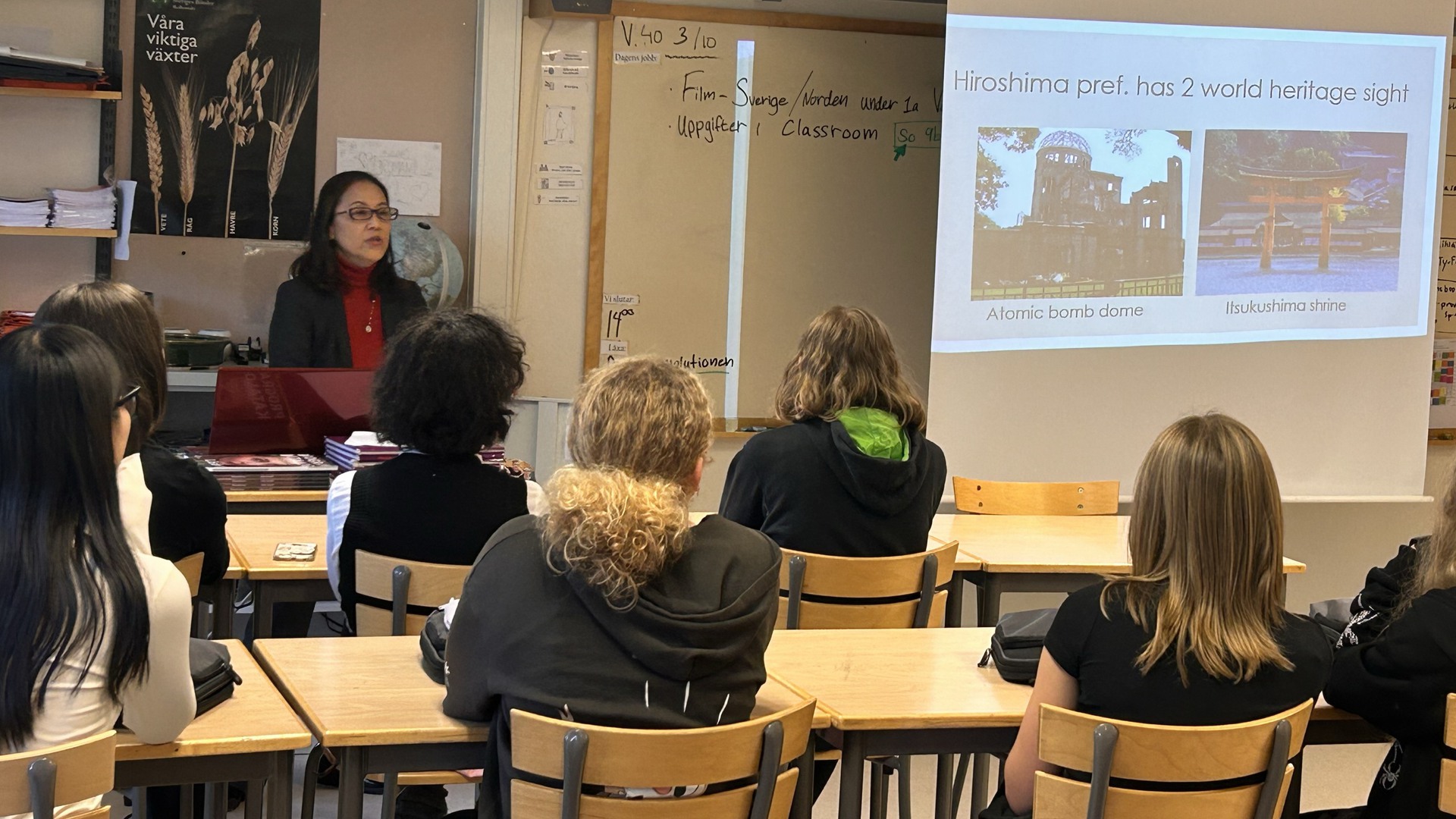 En lärare står framme i klassrummet och undervisar elever som sitter på stolar vid bord. På en projektorduk visas en powerpointpresentation.
