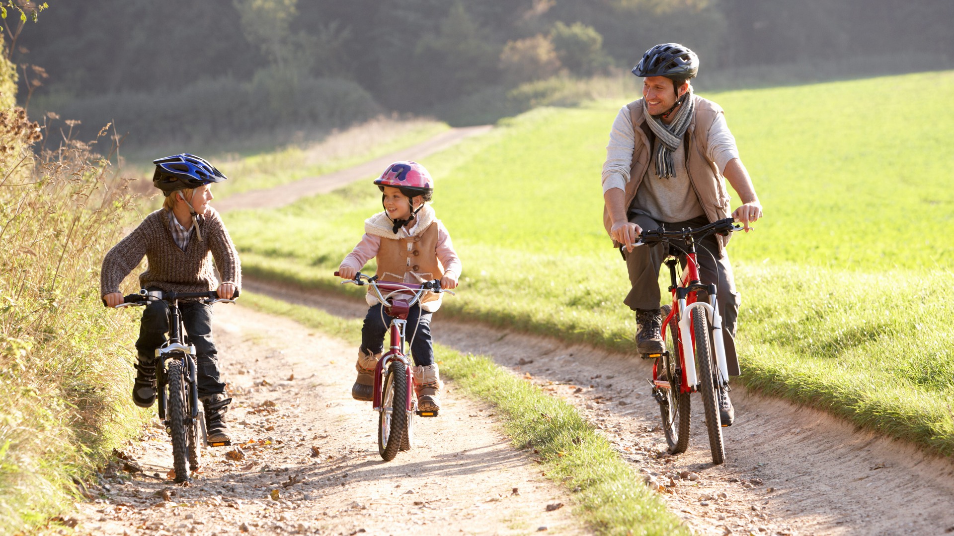 En vuxen och två barn cyklar på en lerig väg. 