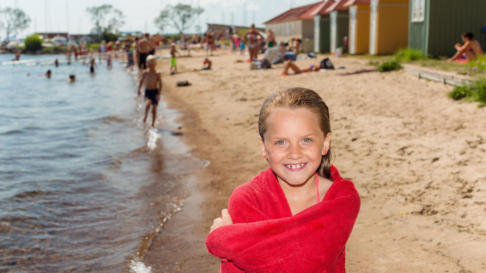Ung tjej i handduk står på stranden vid Guldkroksbadet och ler in i kameran.