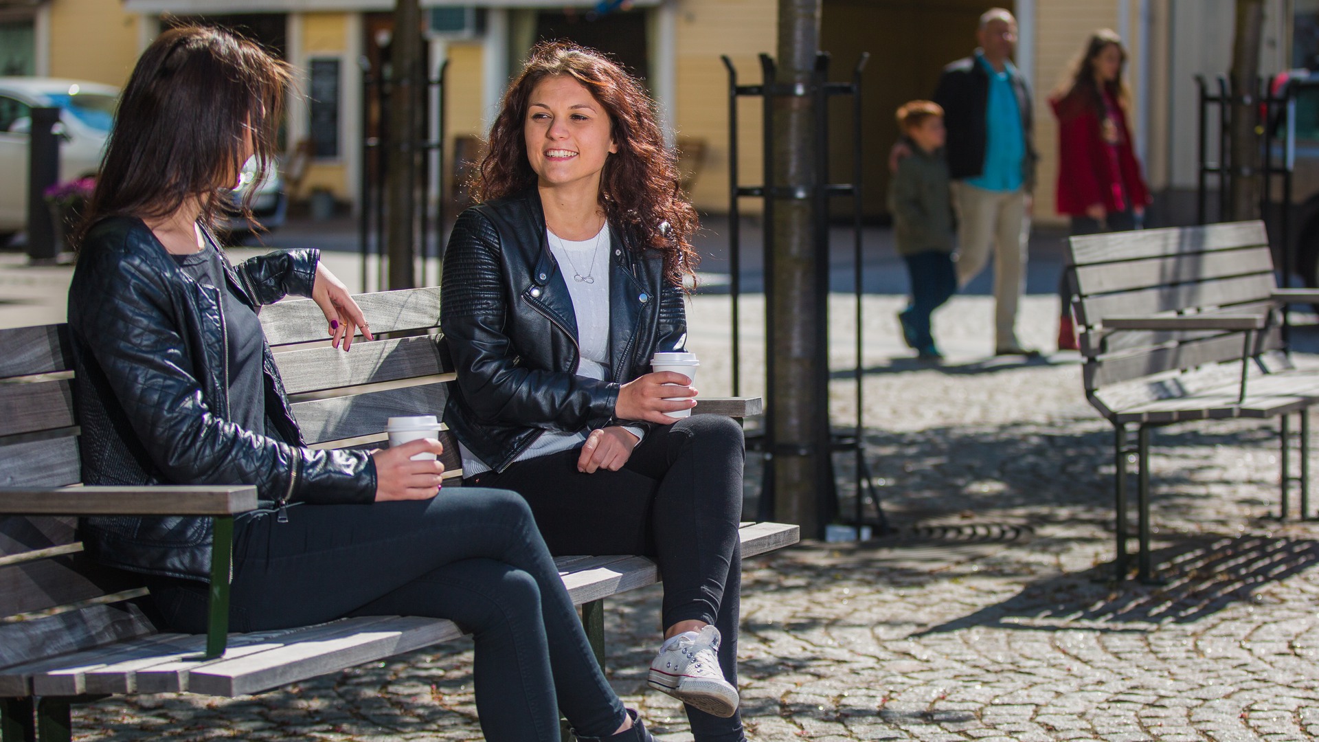 Två unga vuxna dricker kaffe på en bänk vid torget i Hjo.