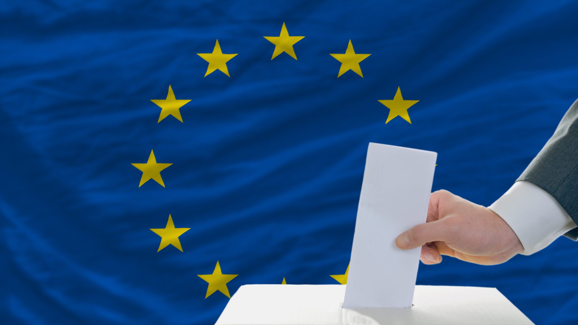 En röstsedel läggs i en låda. I bakgrunden syns EU-flaggan.