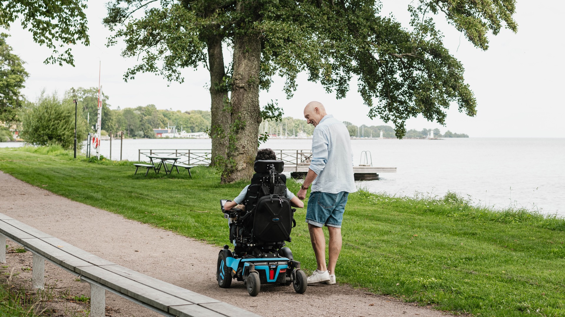Två personer på promenad längs strandpromenaden. En sitter i rullstol.