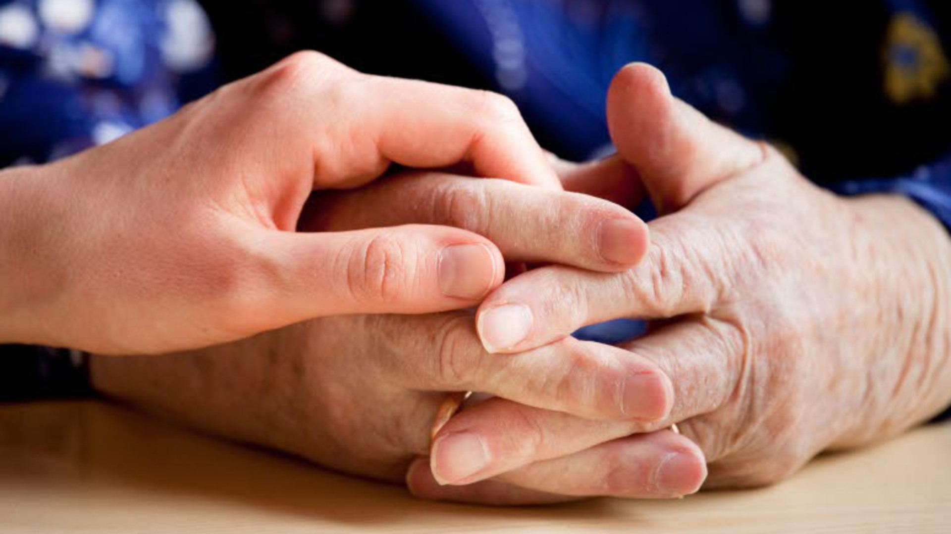En äldre persons händer och en vuxen persons hand som håller ovanpå dem.