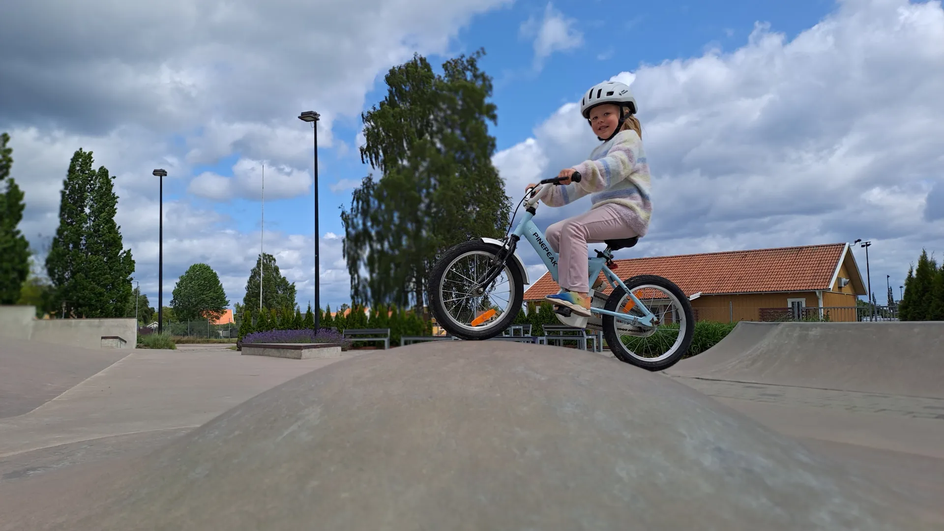 En liten flicka i färgglada kläder som cyklar över ett gupp i Actionparken.