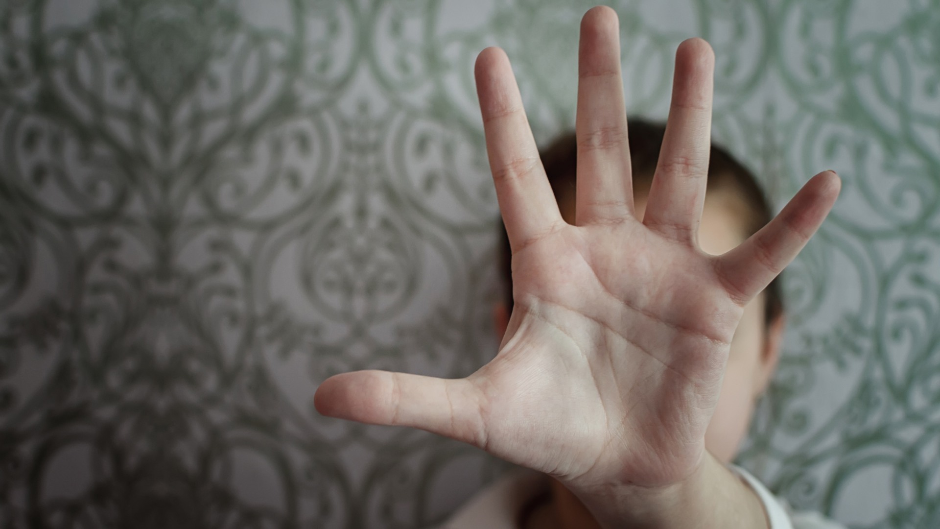 En person håller upp en hand  med handflatan framåt framför sitt ansikte.