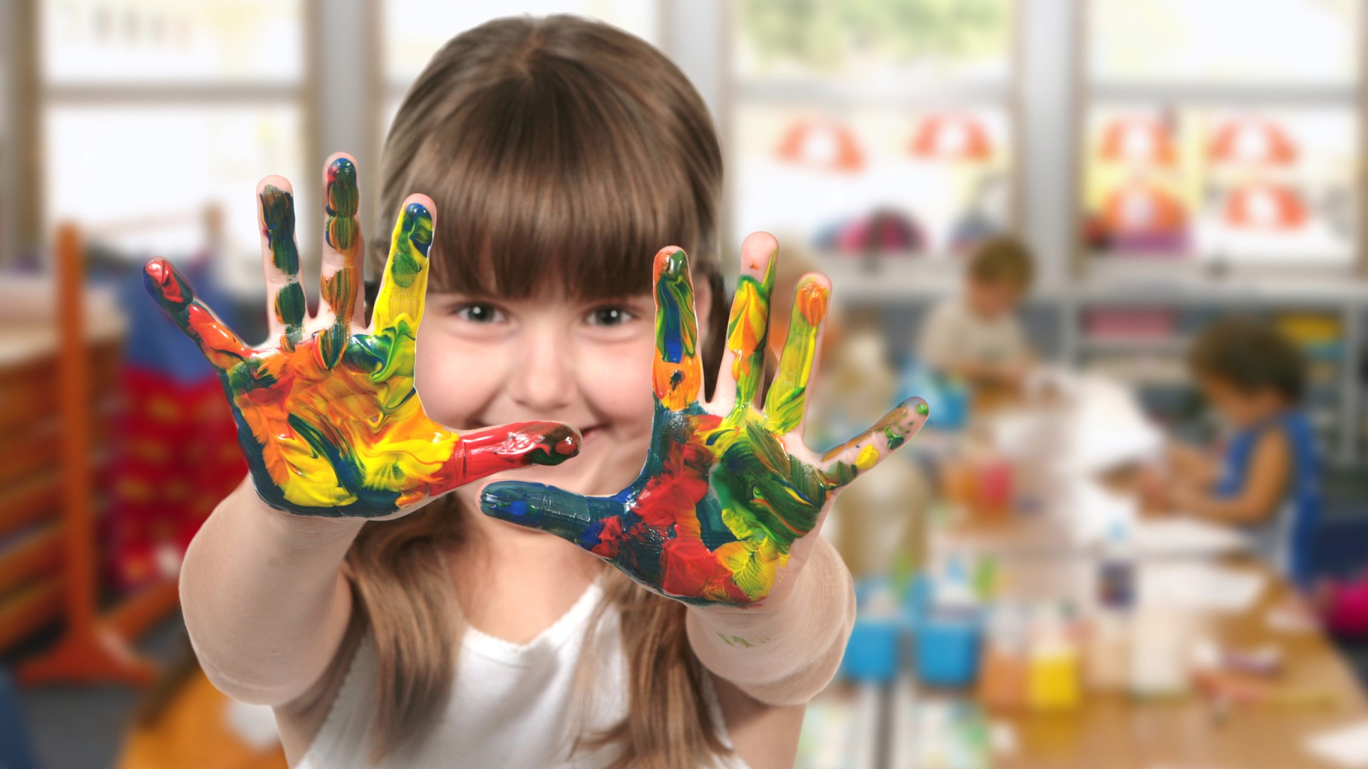 Ett glatt förskolebarn visar upp sina handflator som är fyllda av färg.