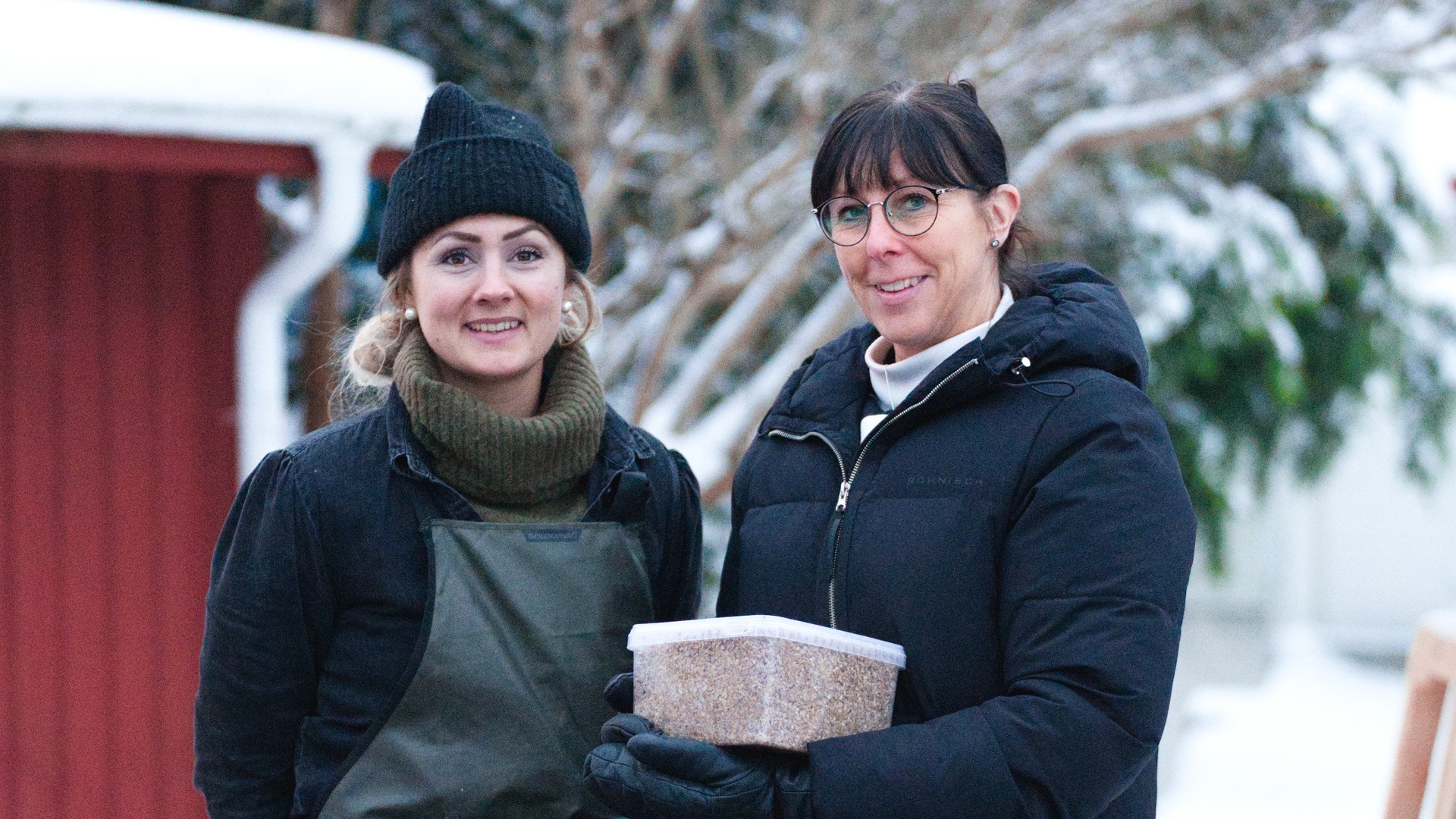 Annika från Hjo bryggeri och Anna från måltidsenheten pratar med varandra ute i snön. Anna håller i en plastburk med drav.