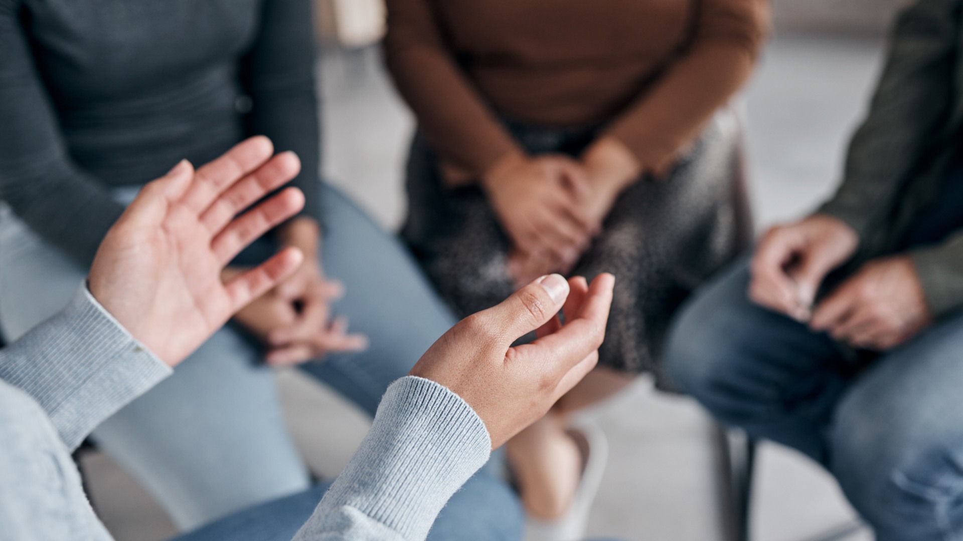 Personer sitter på stolar i en ring. I förgrunden syns en persons händer som gestikulerar.