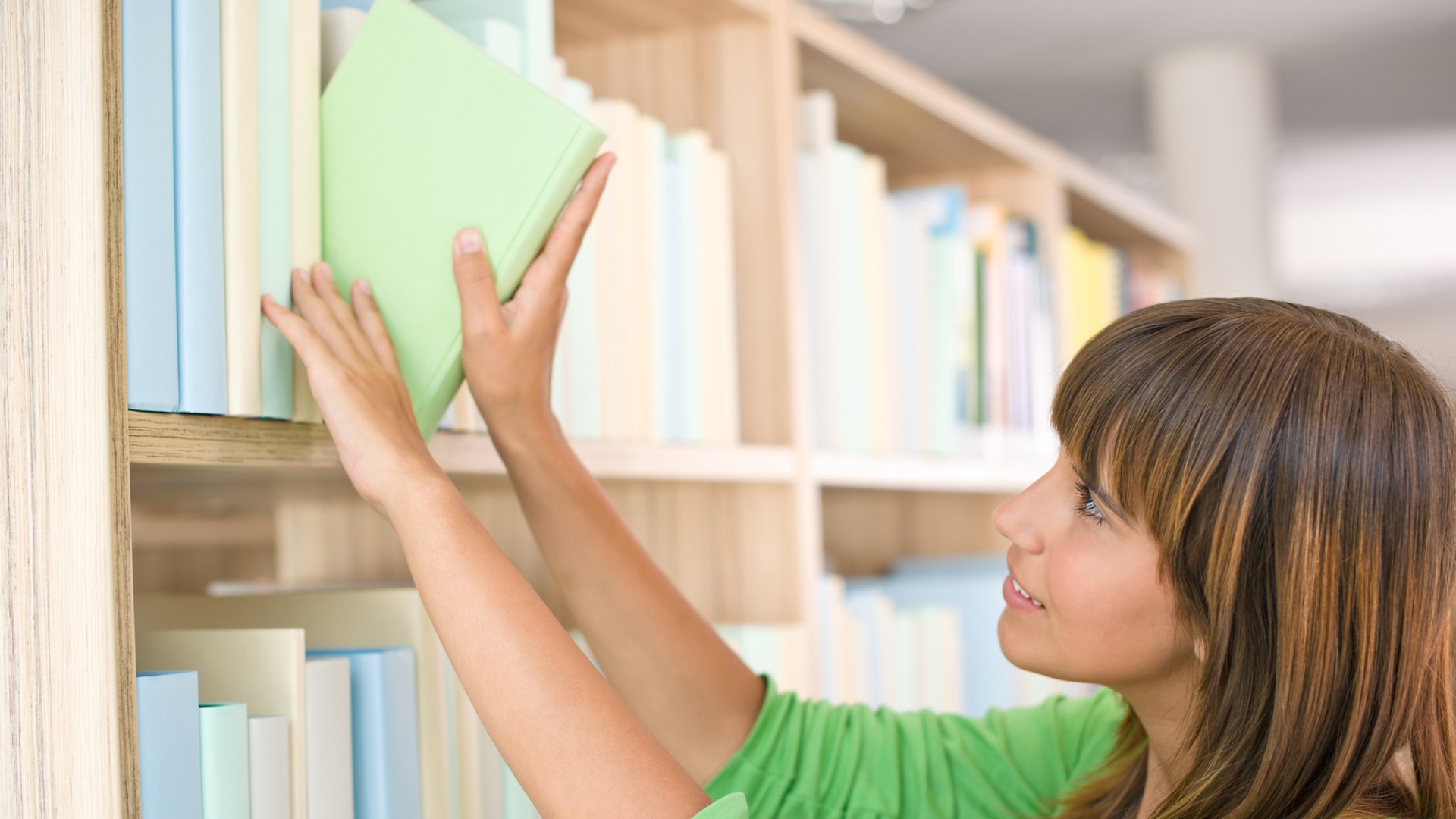 Kvinnan tar en bok från bibliotekets hylla.