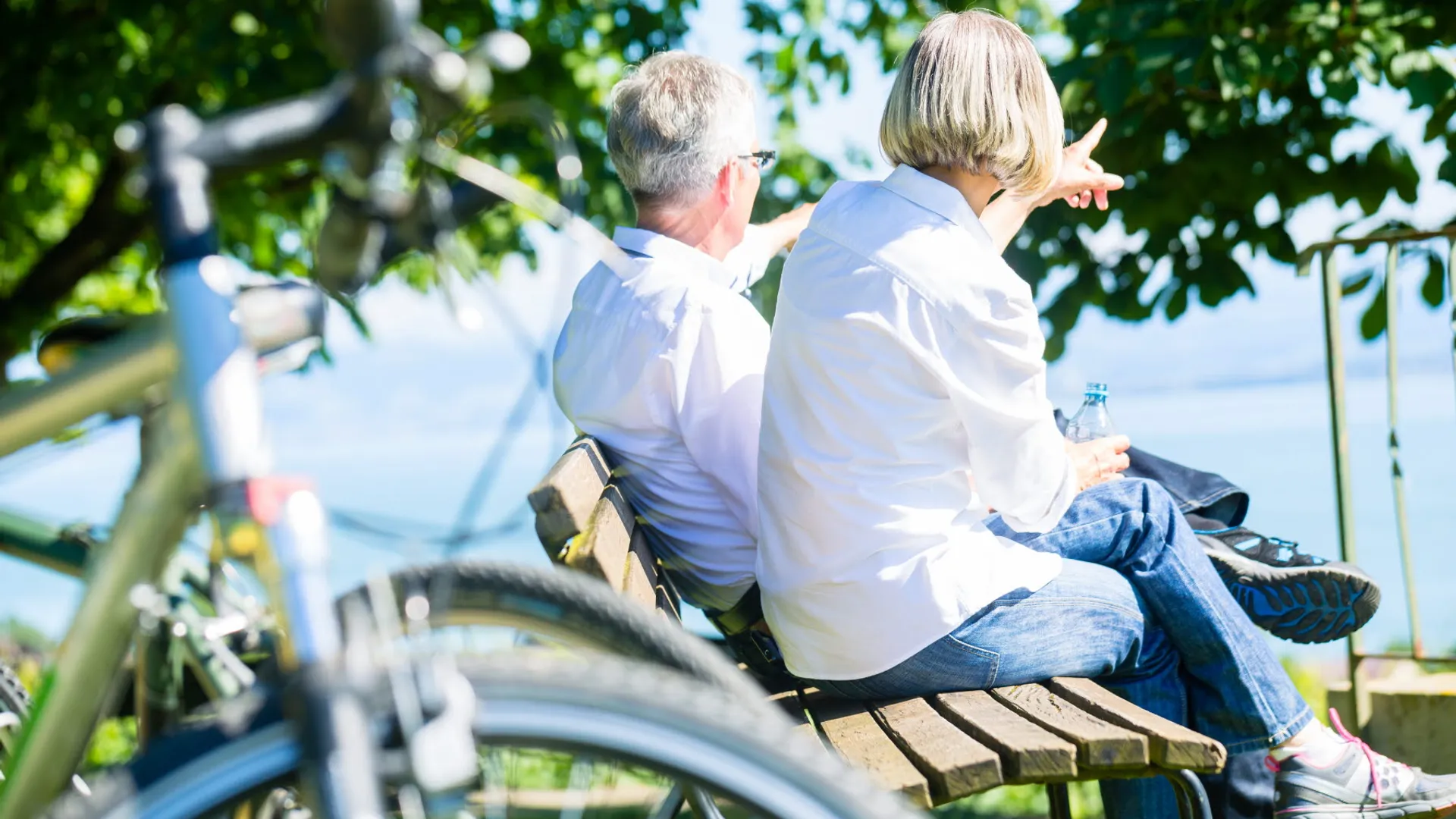 Två vuxna sitter på en bänk och tittar ut över vattnet. En cykel i förgrunden.