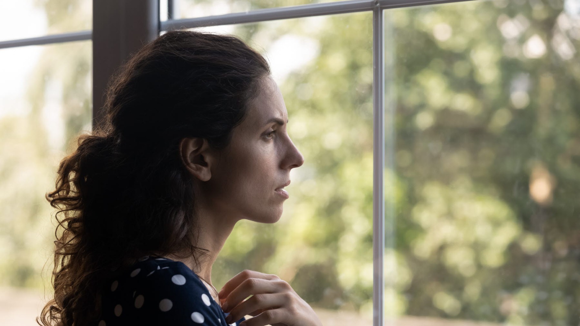 En person tittar ut genom ett fönster och ser sorgsen ut.