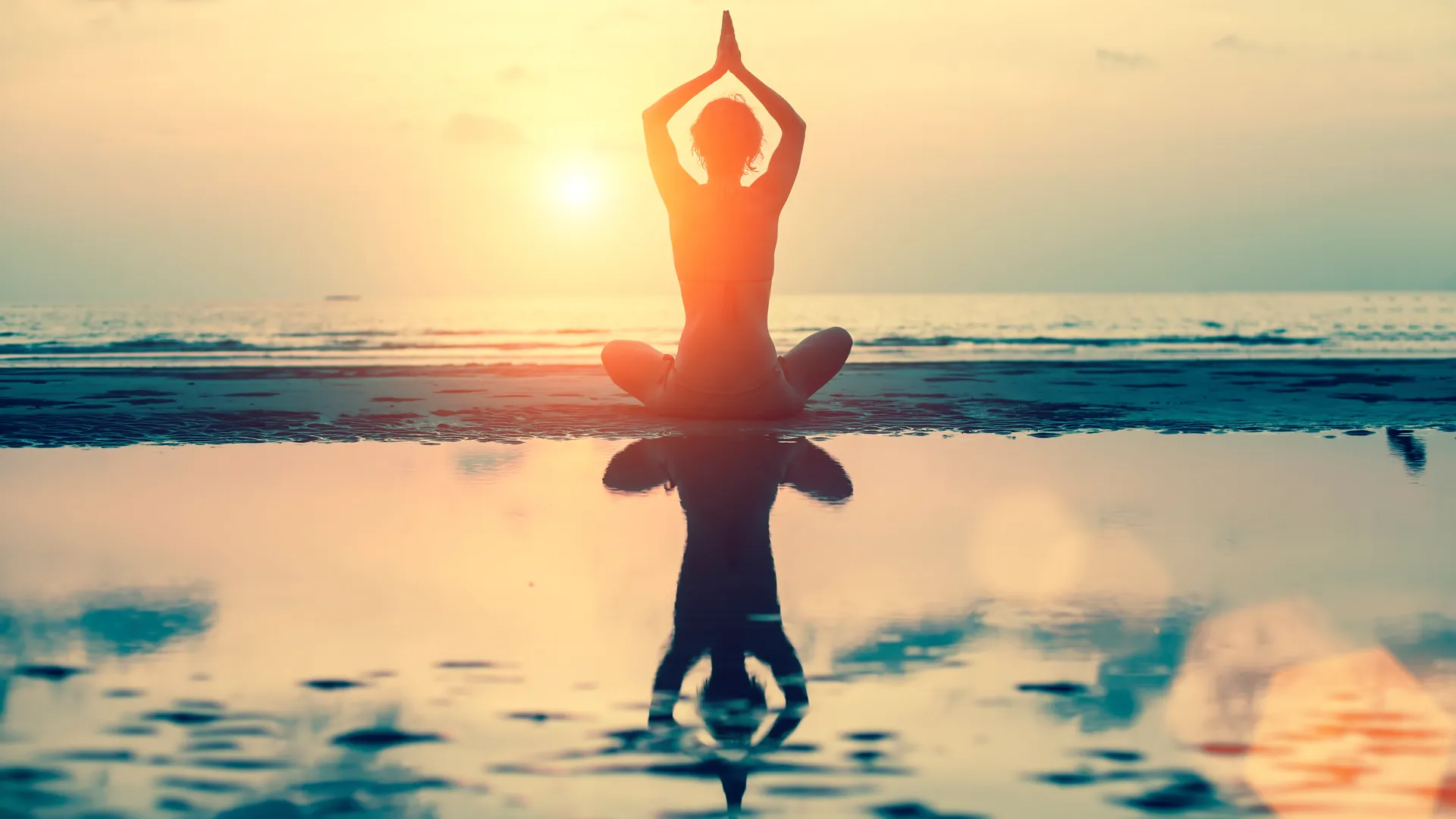 Person som sitter i solnedgång och yogar med vatten framför sig