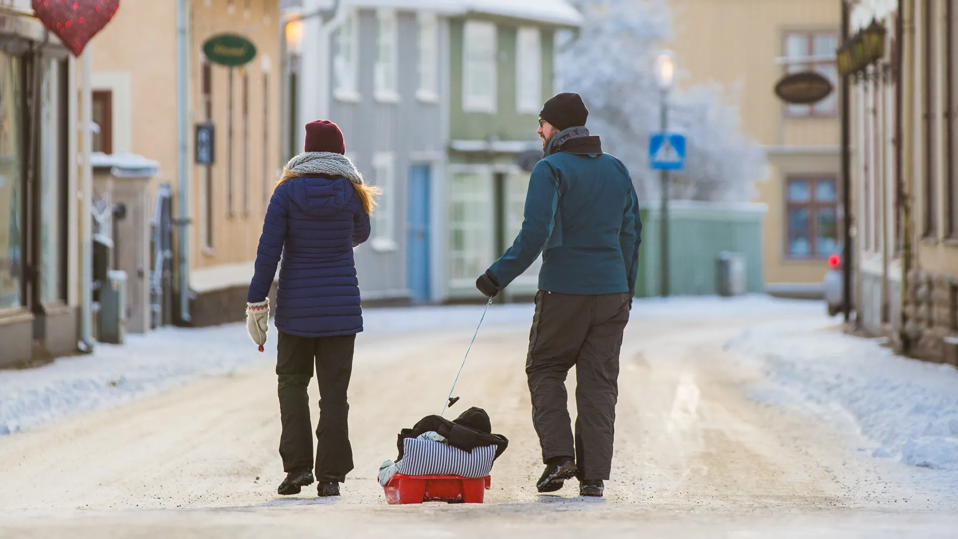 Två personer med barn i en pulka promenerar Långgatan fram.