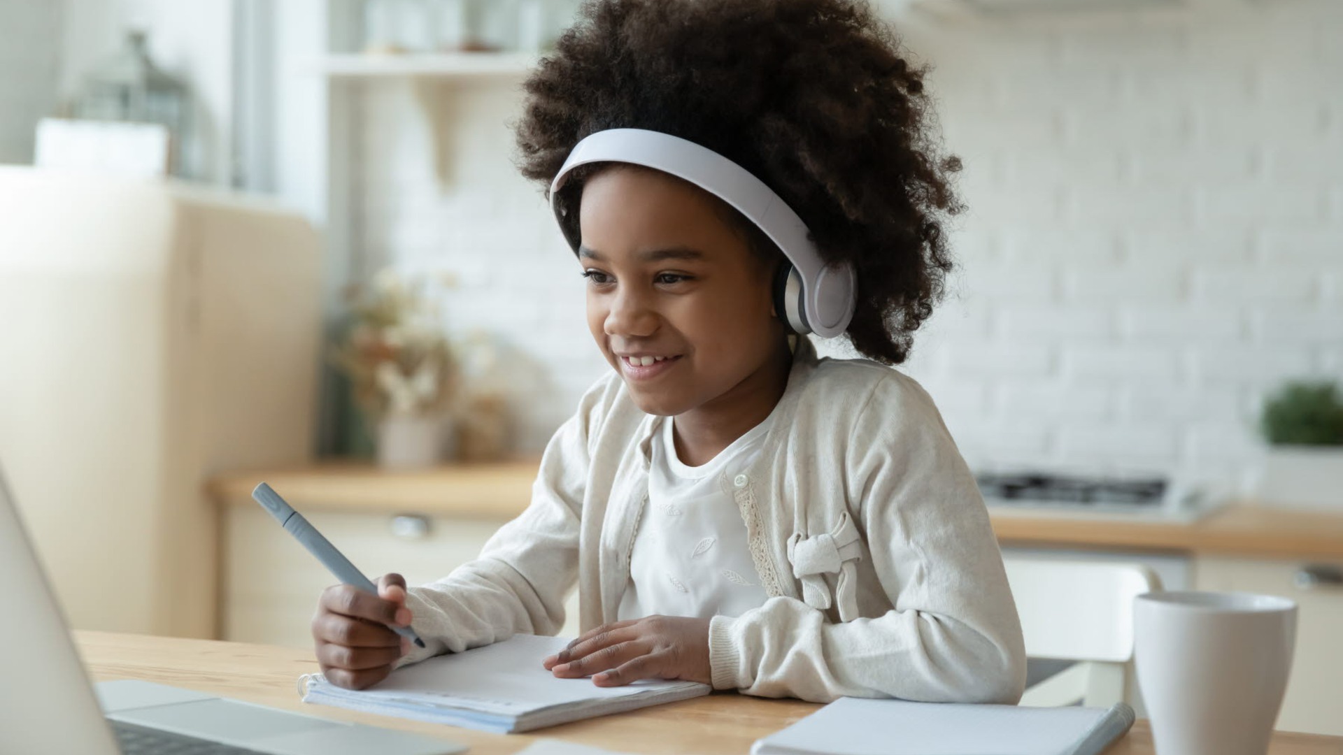 Ett barn sitter framför en dator med hörlurar och papper. Ser glad ut.