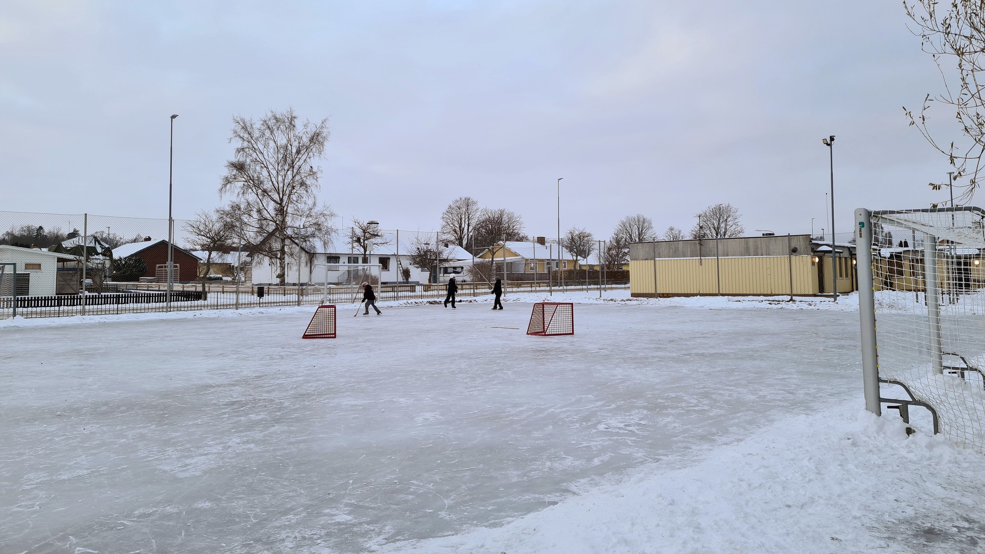 Tre barn åker skridskor på spolad is utanför Guldkroksskolan.