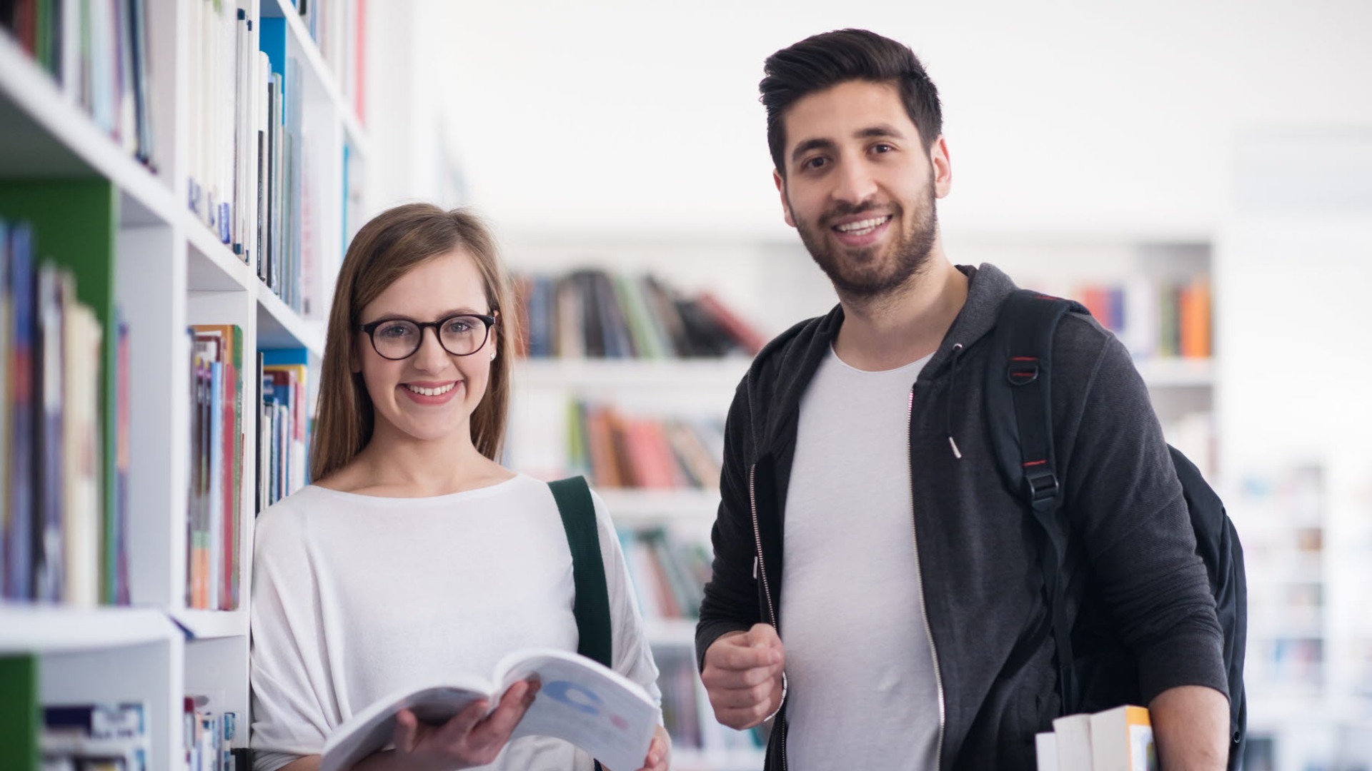 Två personer står i ett bibliotek och håller i böcker.