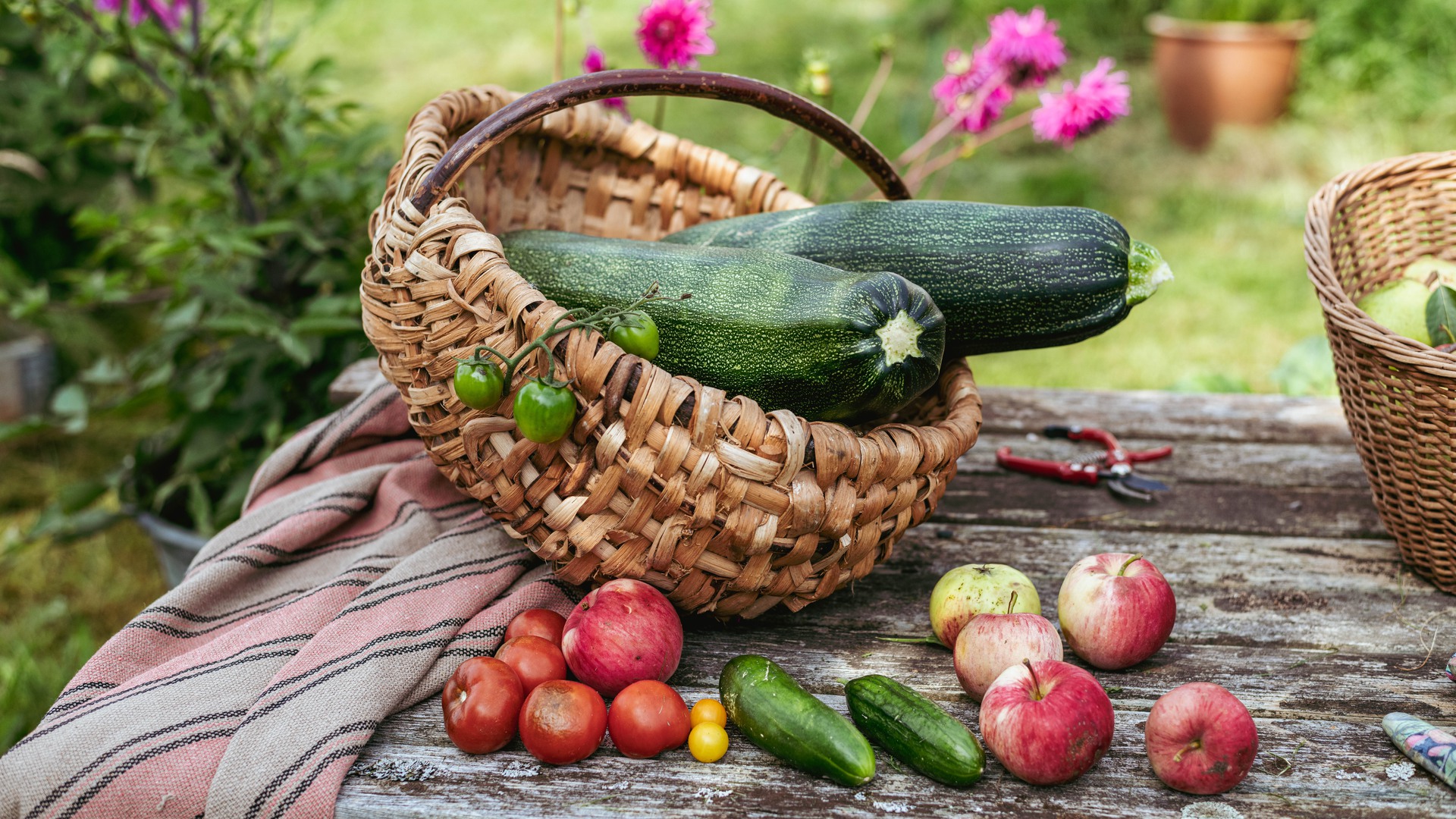 Zucchini och andra grönsaker i en korg på ett träbord utomhus.