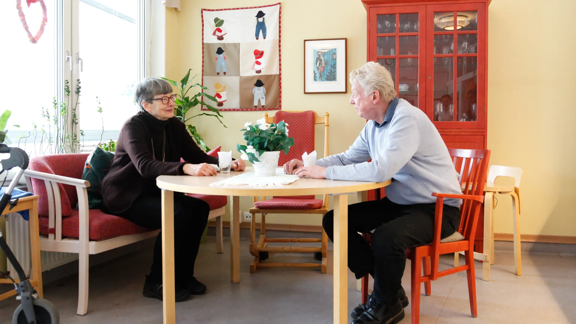 Två äldre personer sitter vid ett bord och samtalar. 
