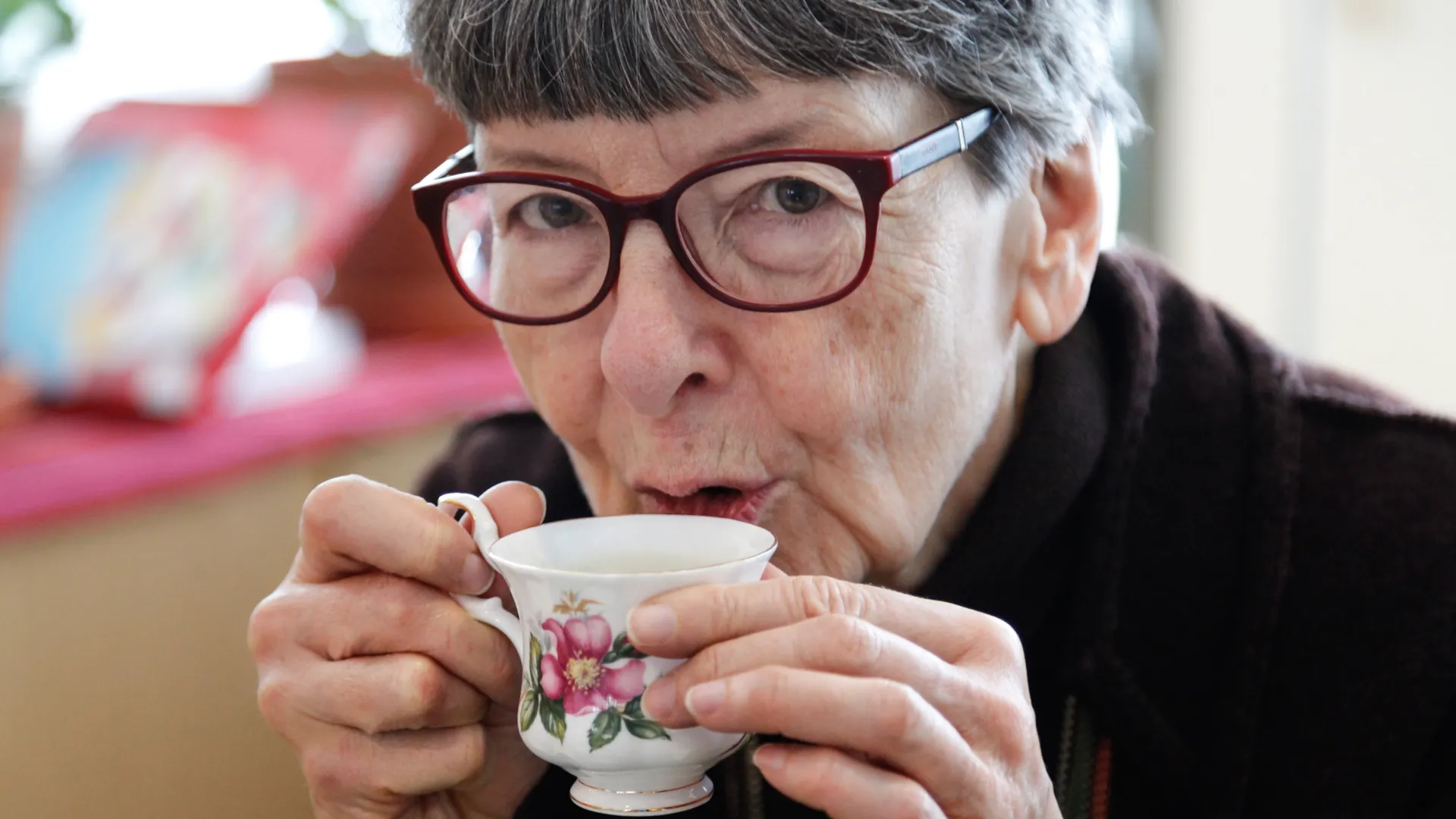 Äldre kvinna dricker kaffe ur en liten kopp.