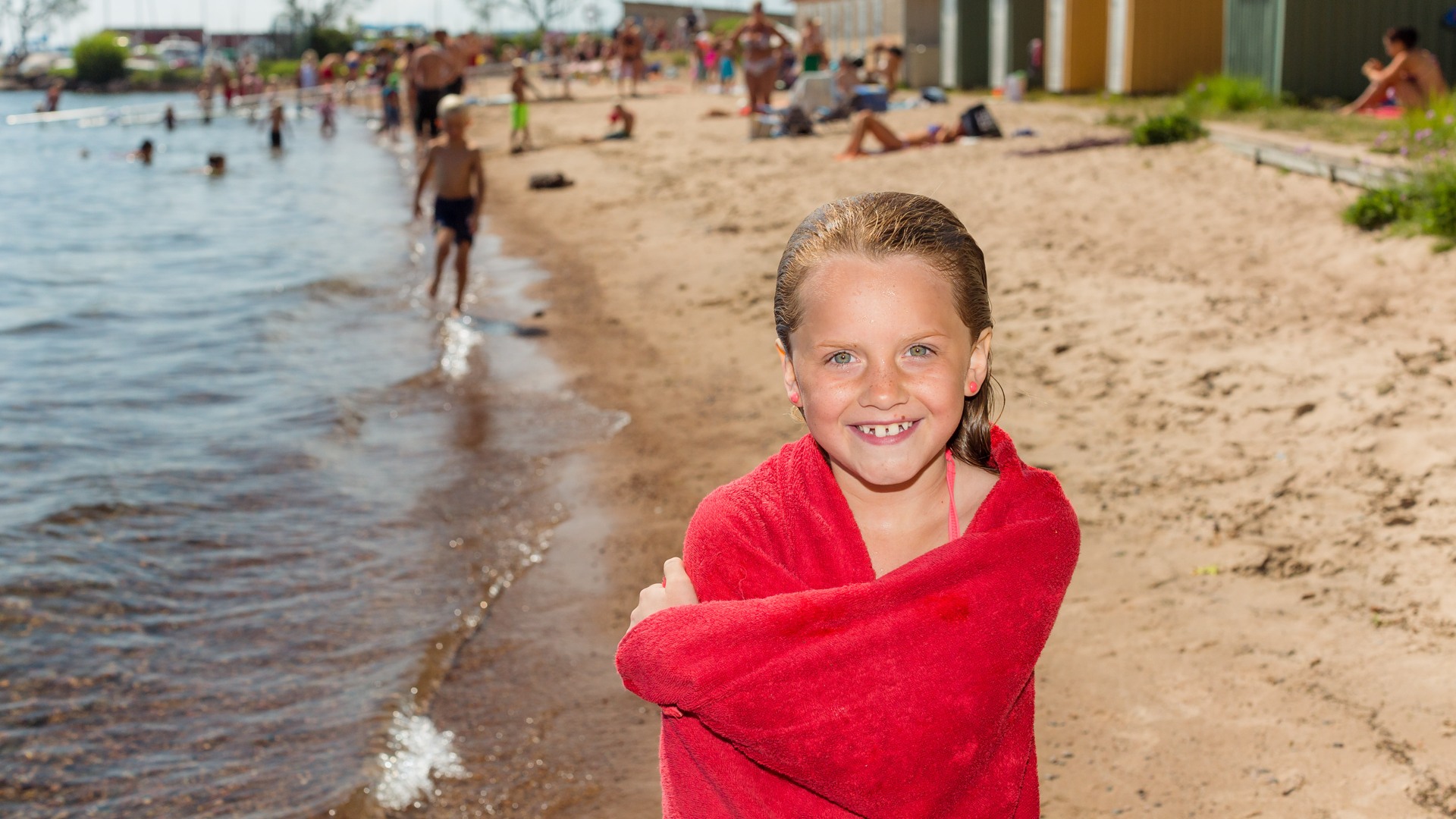 Ung tjej i handduk står på stranden vid Guldkroksbadet och ler in i kameran.