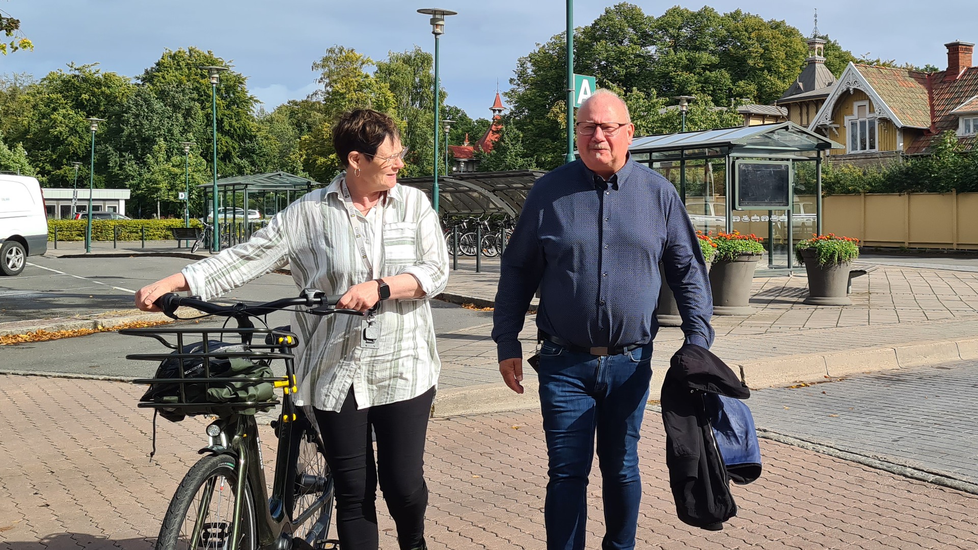 Kommundirektör Eva går med sin cykel vid busstationen, bredvid henne går fastighetschef Bo Adler.