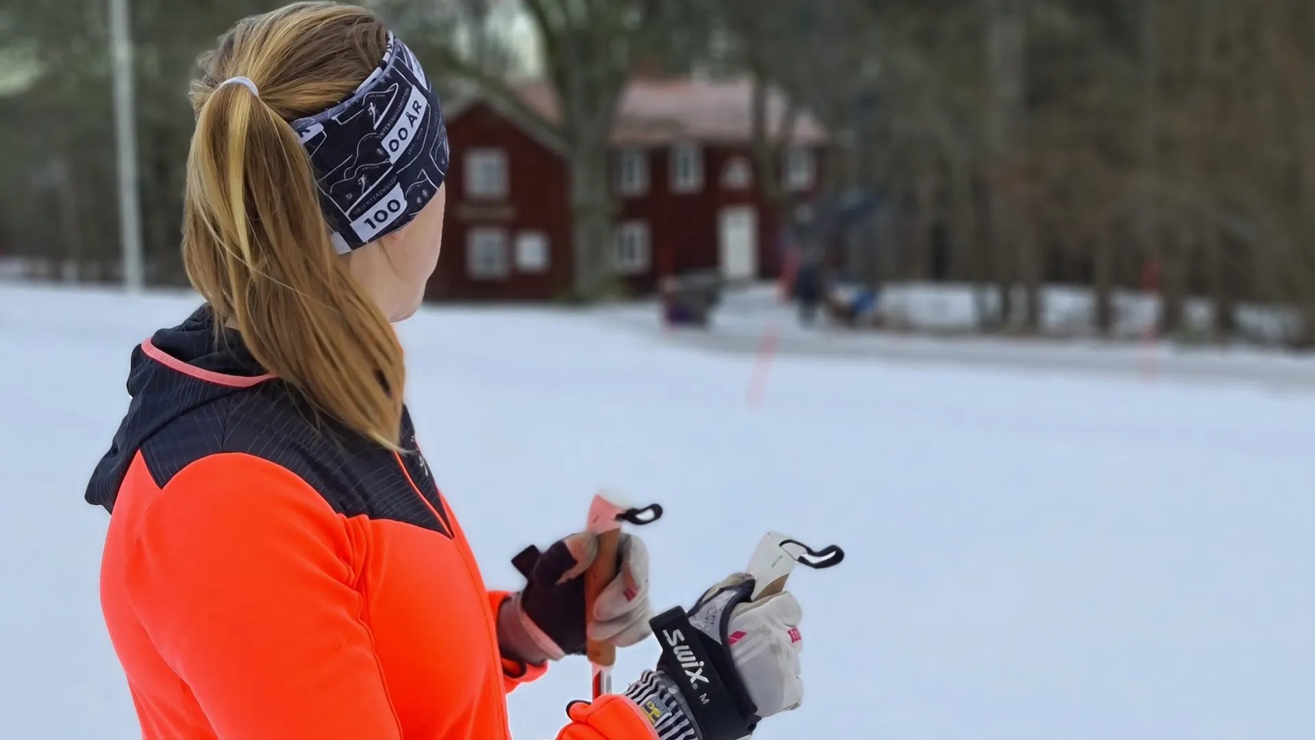 Skidåkare i orange jacka på Högaliden. I bakgrunden syns en röd stuga och det är snö på marken.