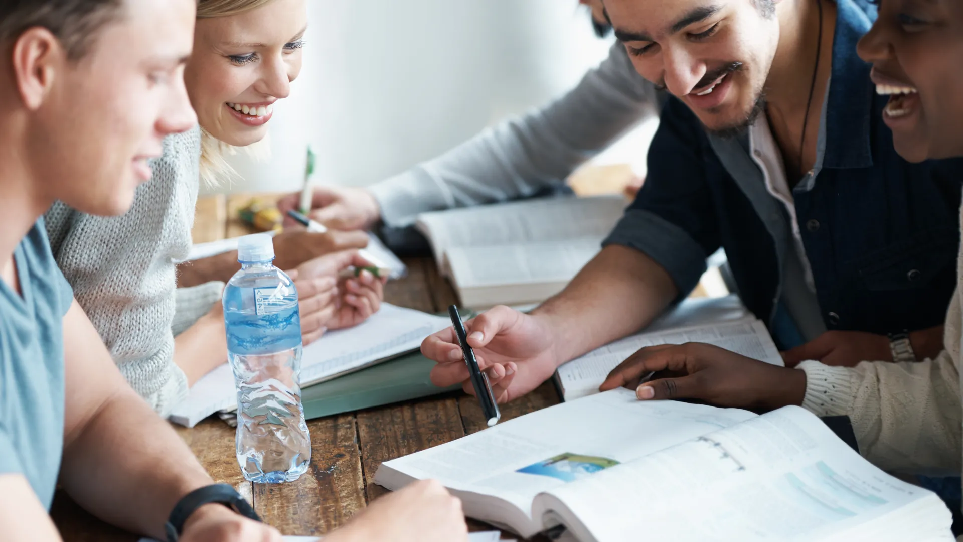 Fem vuxna runt ett bort med böcker och pennor i hand. Studenter som tillsammans studerar ett ämne. 