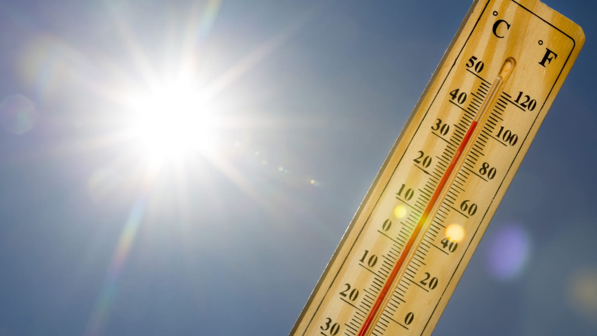 En termometer visar 38 grader, i bakgrunden syns blå himmel och solen.