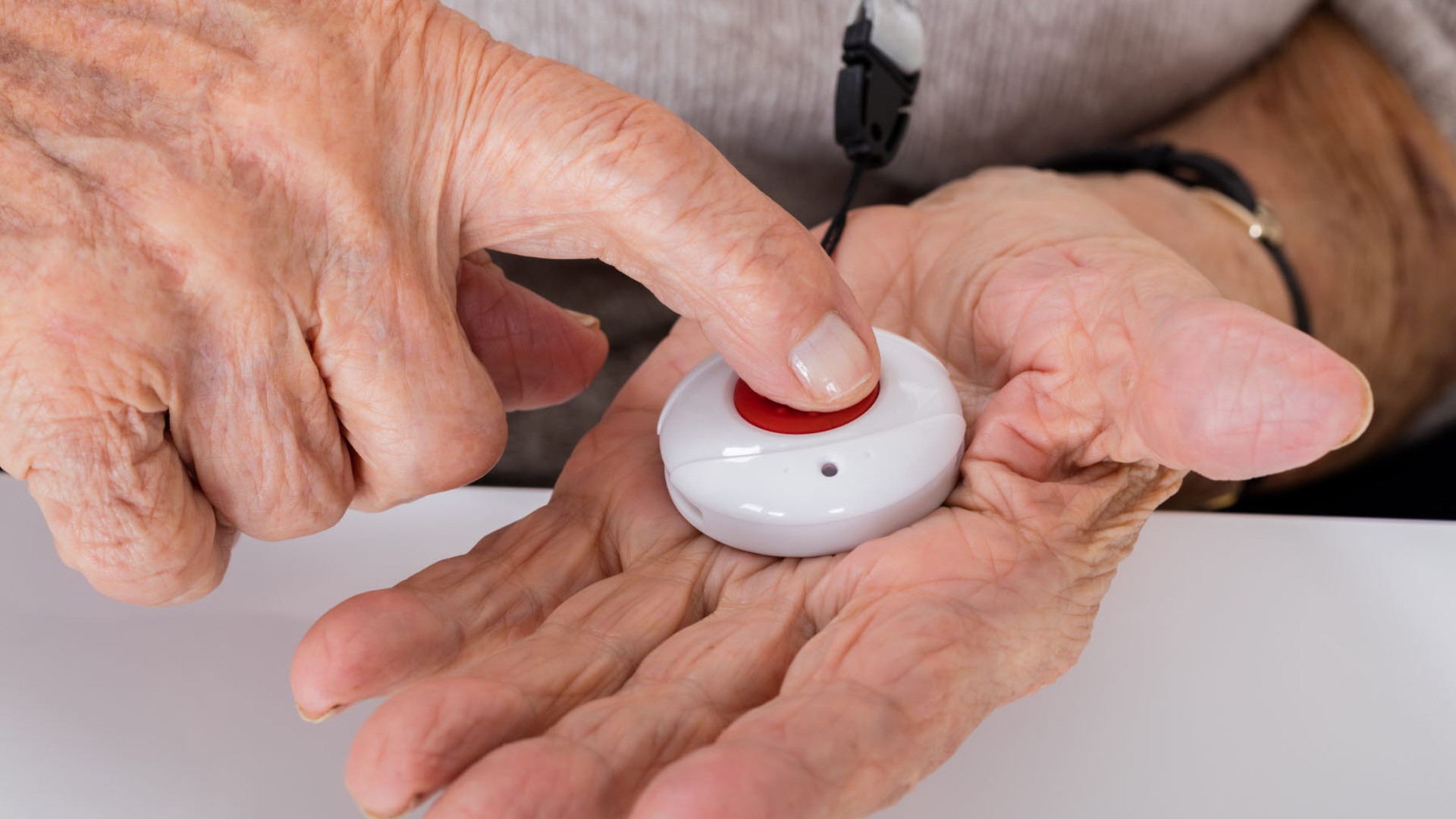 En äldre person trycker på sitt trygghetslarm, en röd knapp.