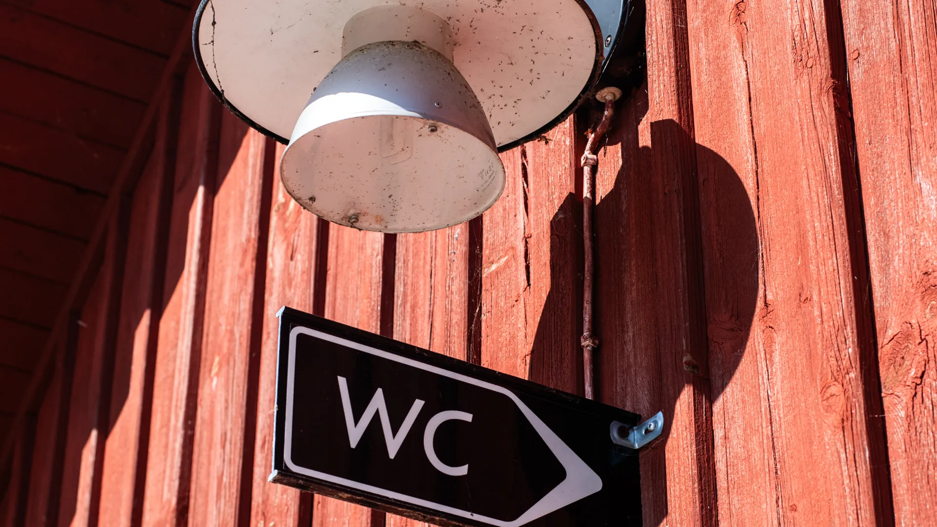 Skylt med texten "WC" på en röd fasad.