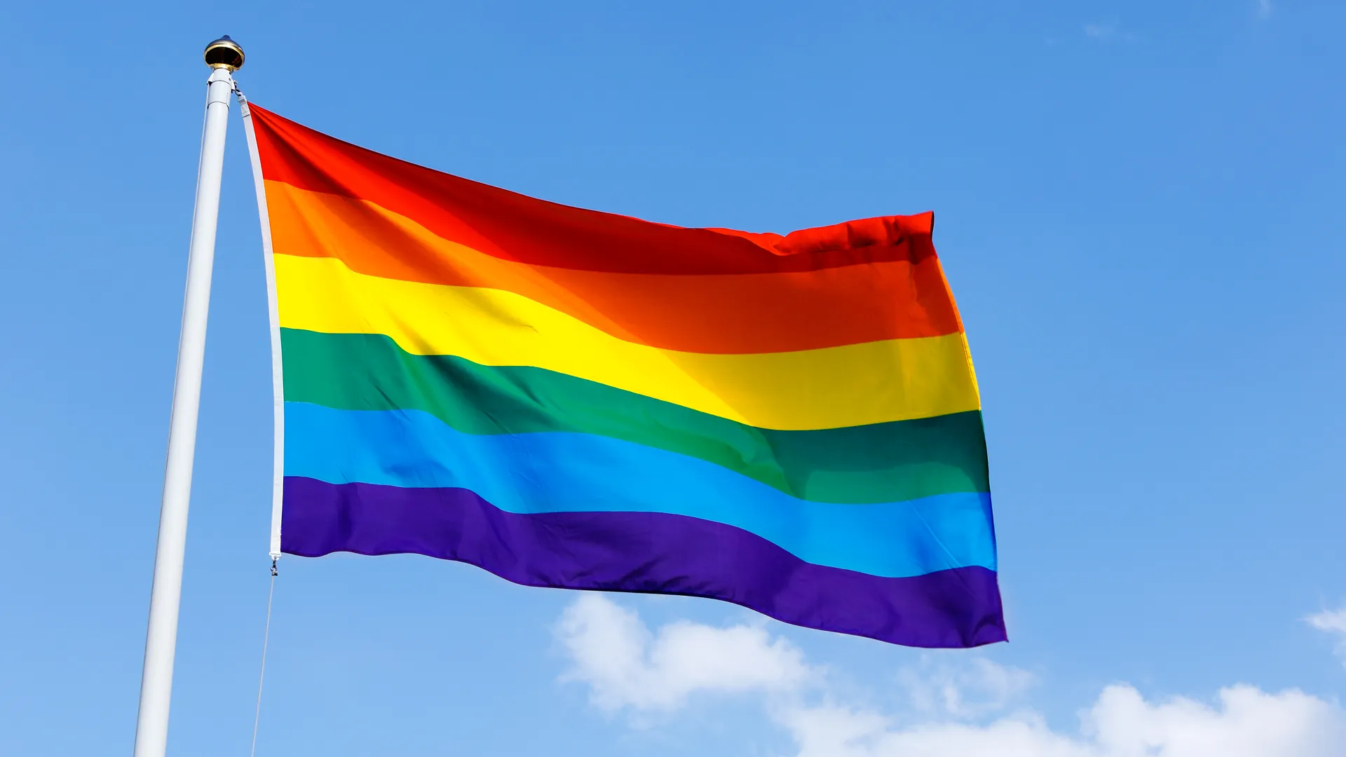 Regnbågsflagga vajar mot blå himmel.