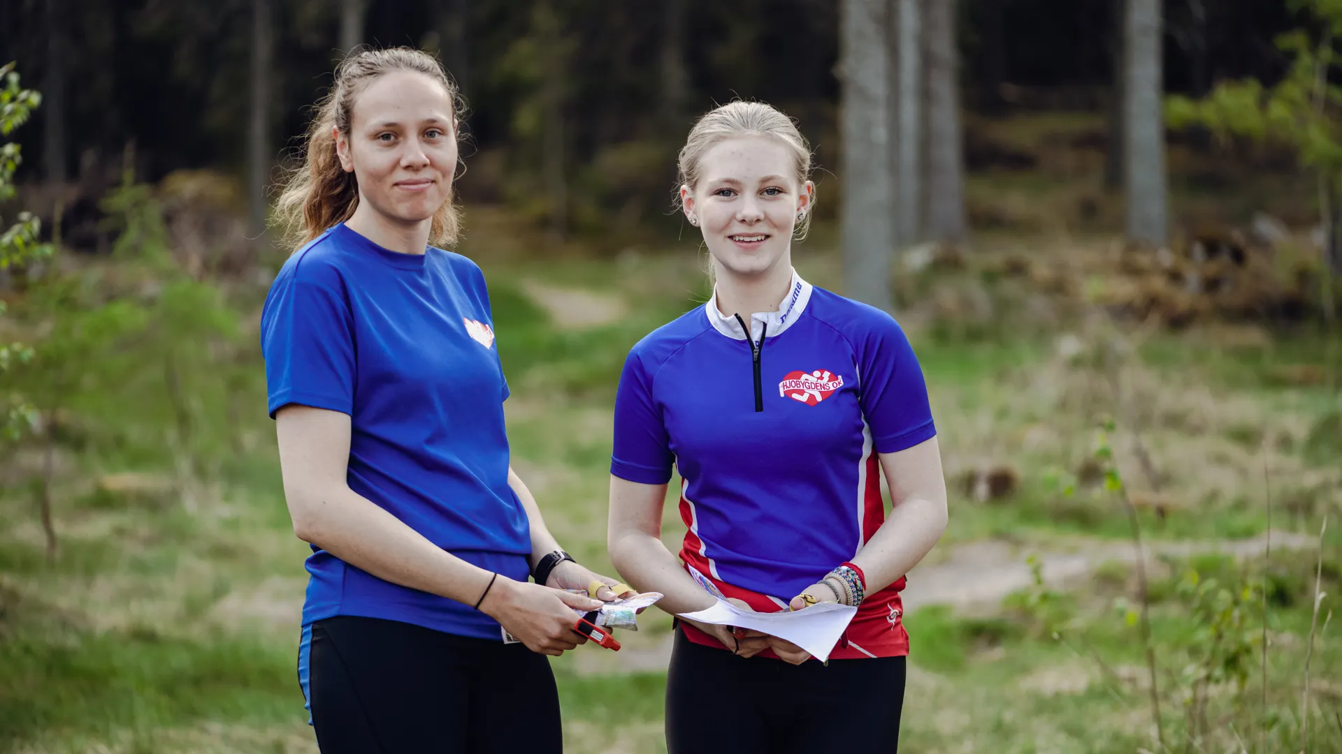Två personer i skogen med varsin orienteringskarta.