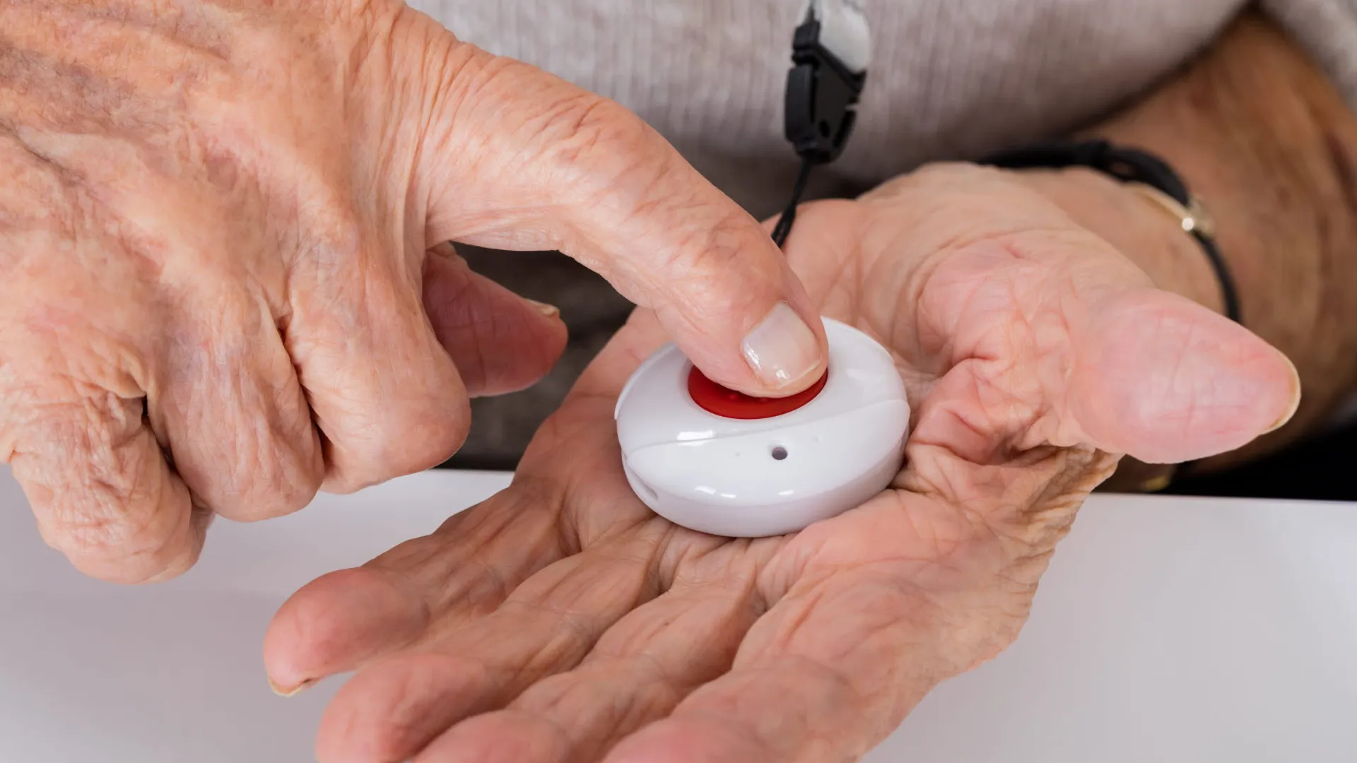 En äldre person trycker på sitt trygghetslarm, en röd knapp.