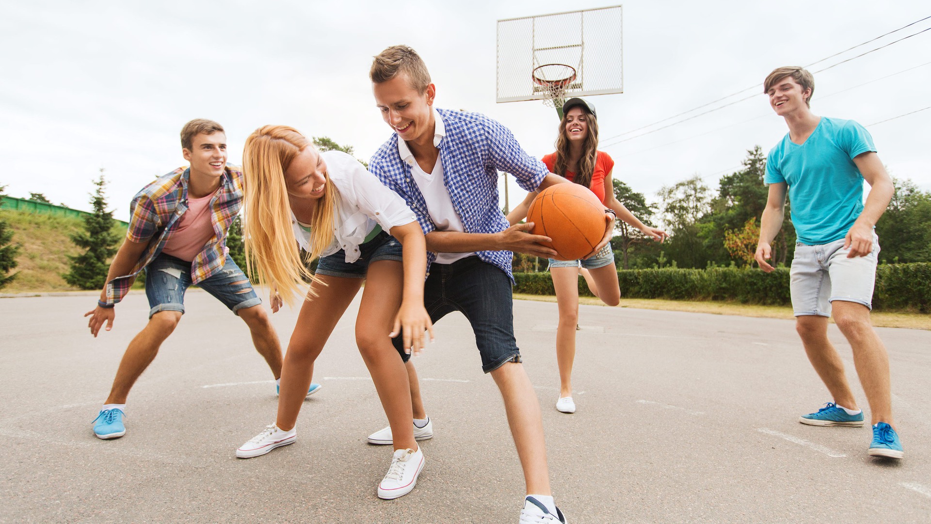 Ungdomar spelar basket tillsammans utomhus.