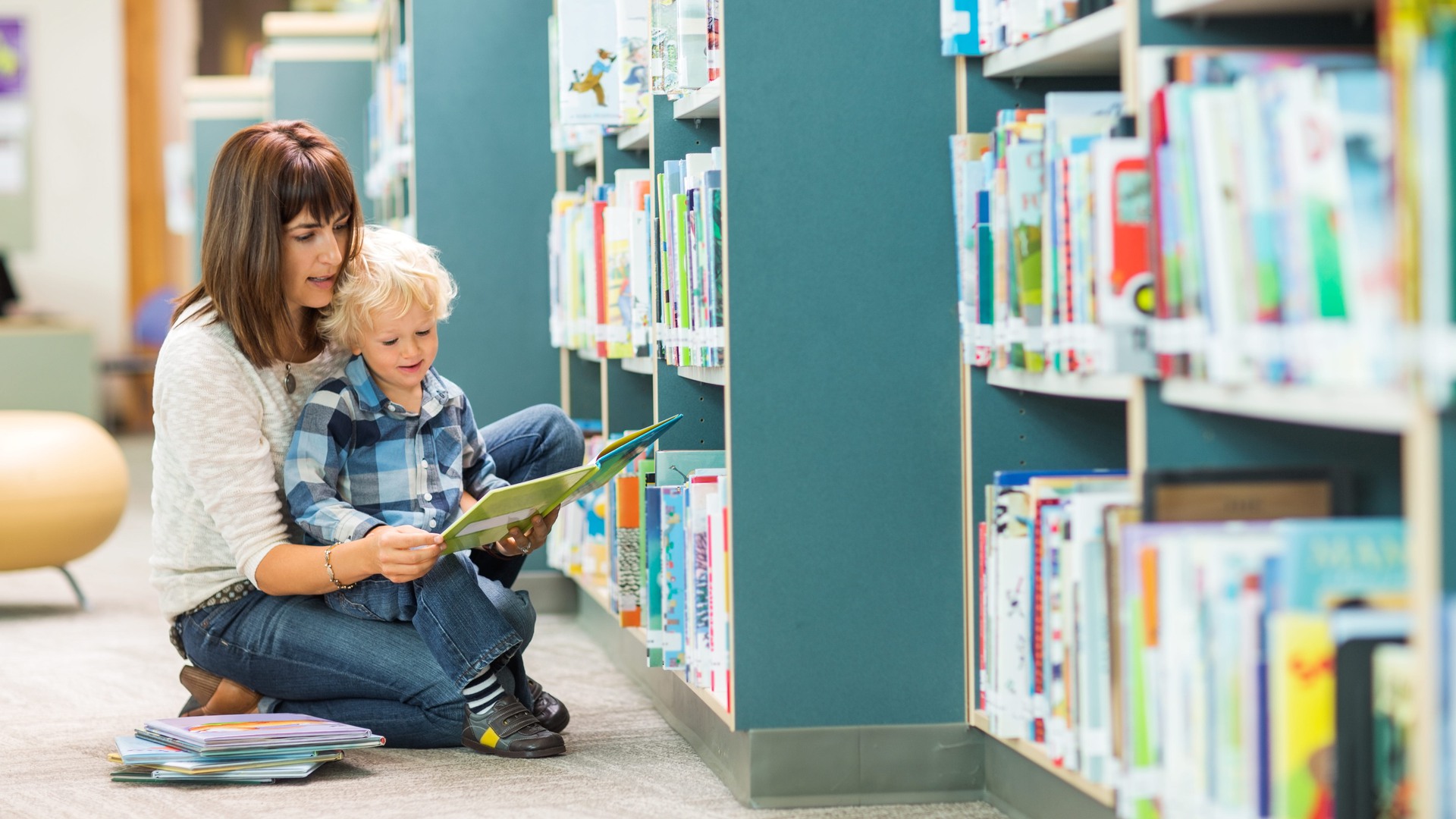 En vuxen sitter med ett barn i knät i ett bibliotek.