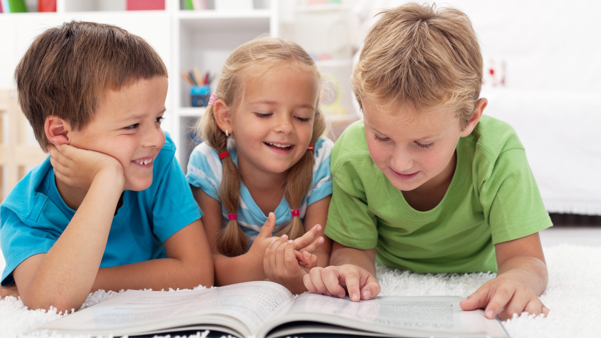 Tre förskolebarn ligger på golvet och läser i en tidning. 