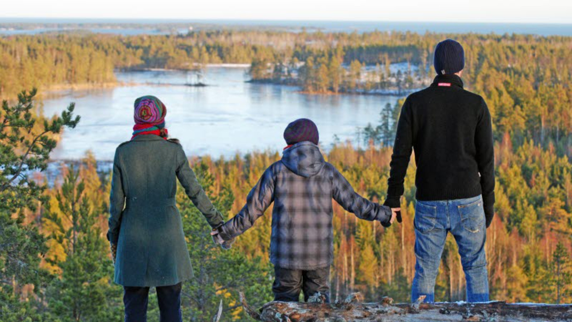 Tre personer håller varandra i händerna och tittar ut över ett höstlandskap och en sjö.