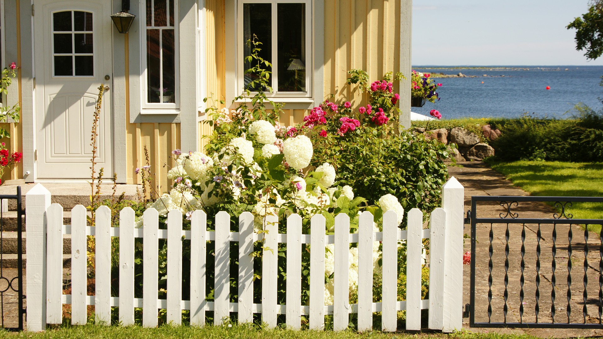 Ett gult trähus vid vattnet, med ett vitt staket framför.