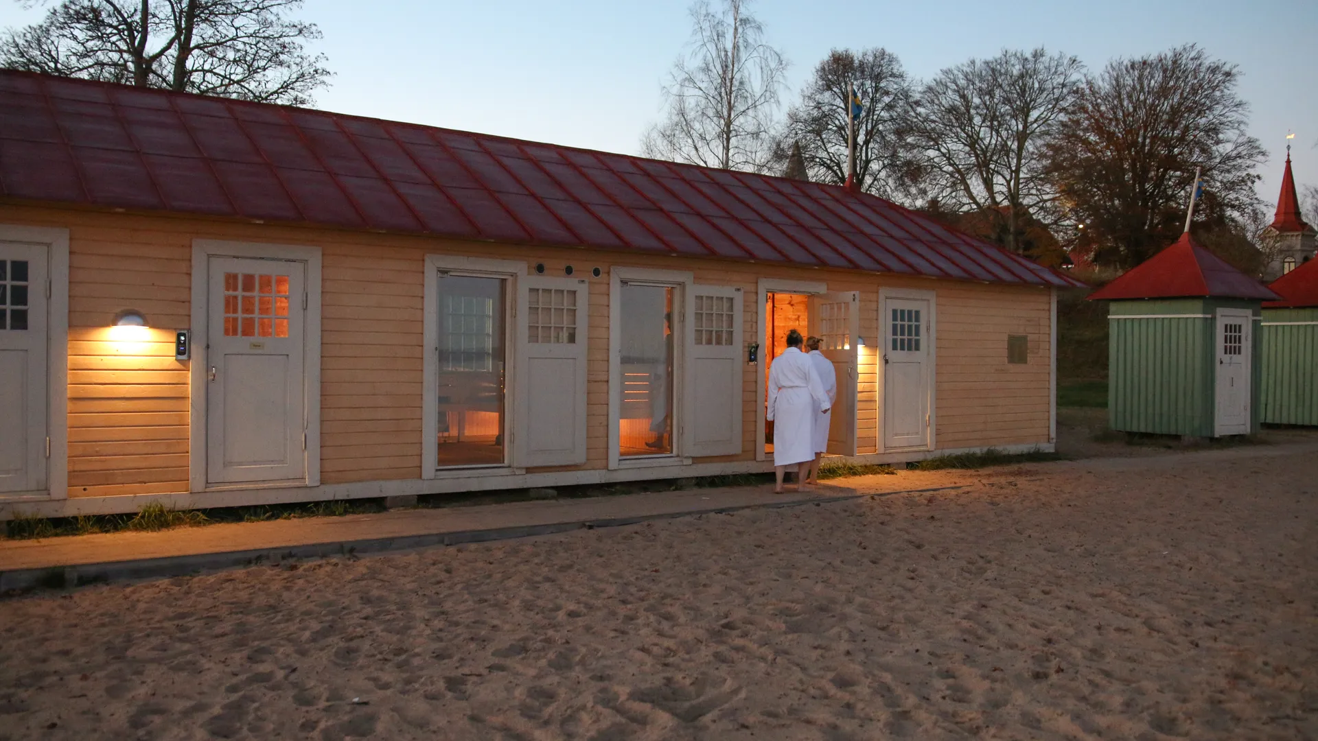 Två personer som går in i badhyttsbastun på stranden i Hjo.