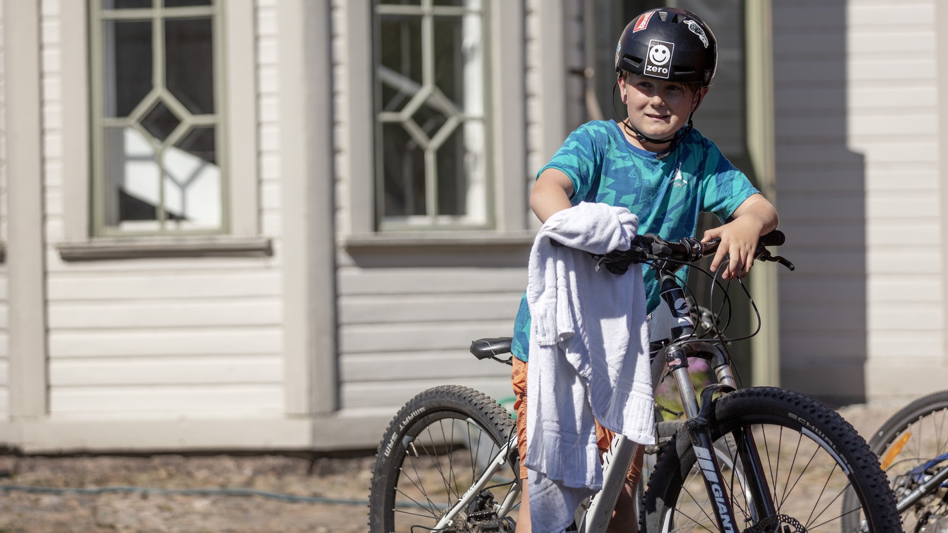 Ett barn står med sin cykel framför ett trähus.