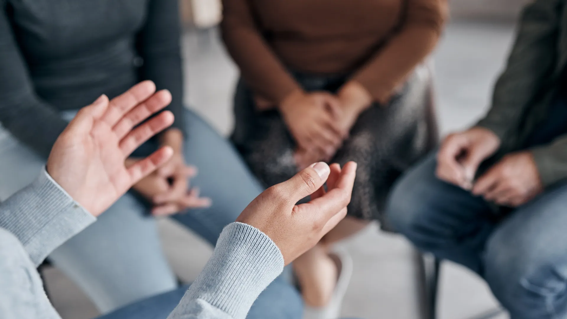 Personer sitter på stolar i en ring. I förgrunden syns en persons händer som gestikulerar.