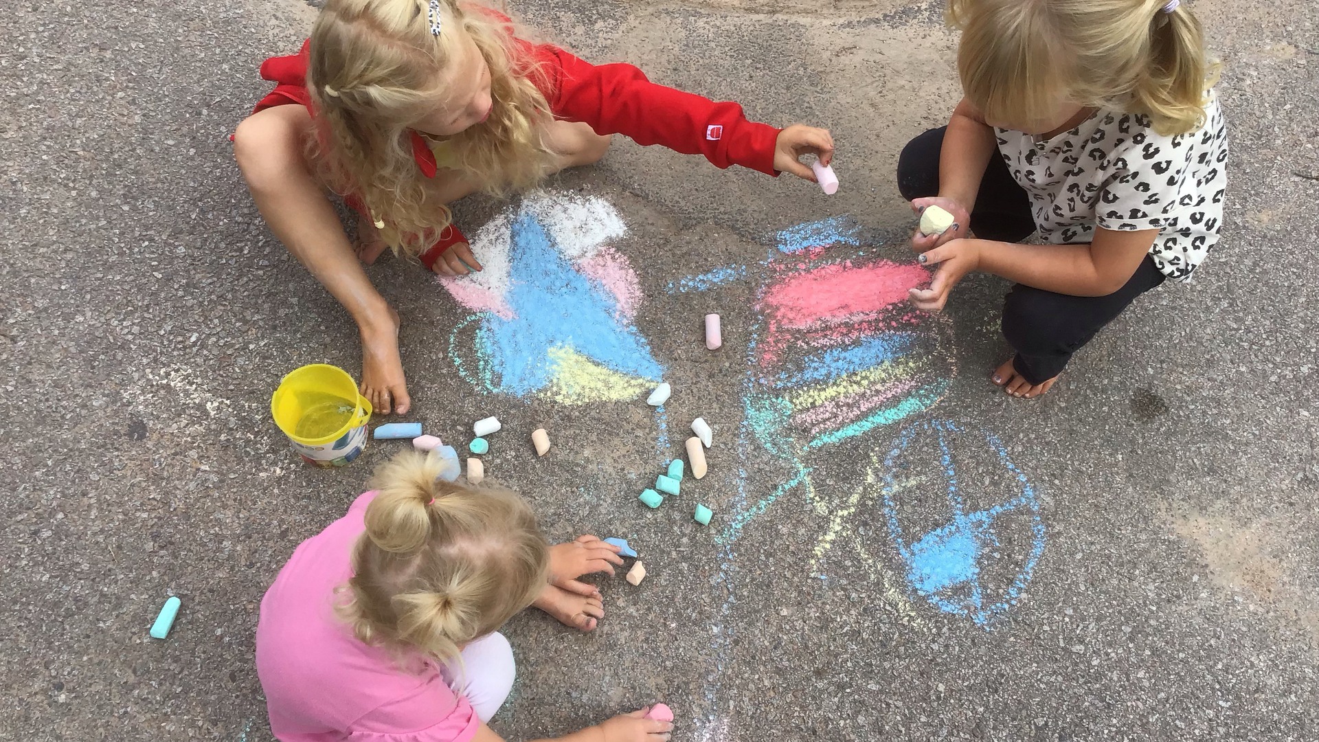 Tre barn målar med gatkritor.