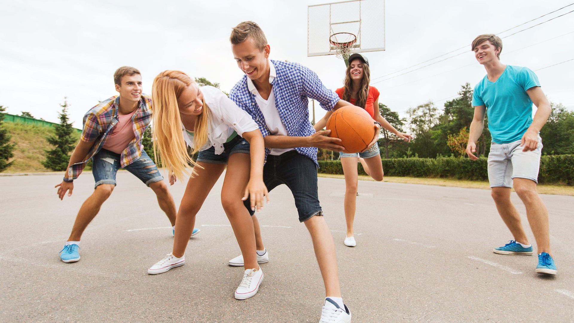 Ungdomar spelar basket tillsammans utomhus.