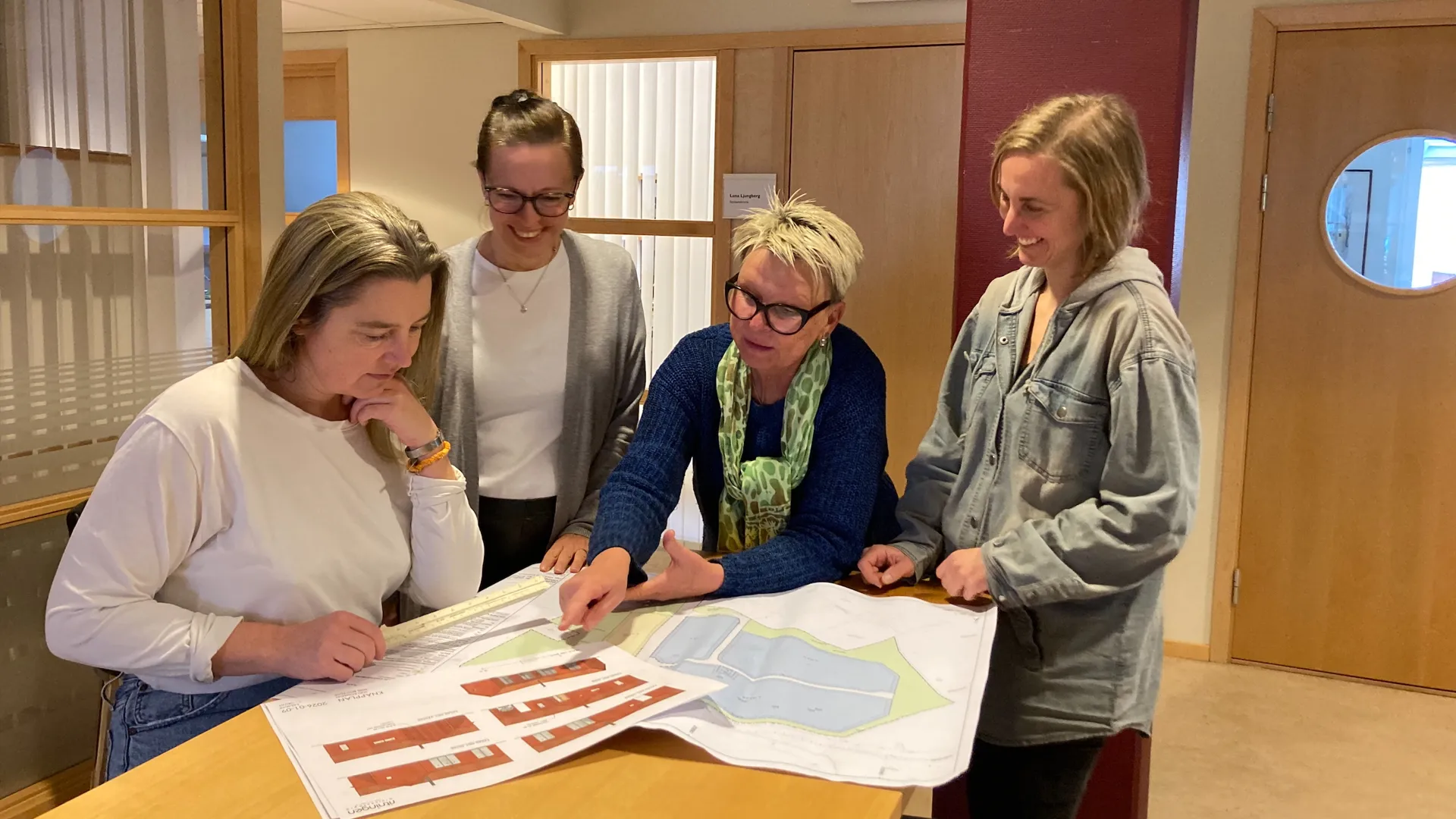 Fyra bygglovshandläggare står runt ett bord och tittar på kartor och ritningar.