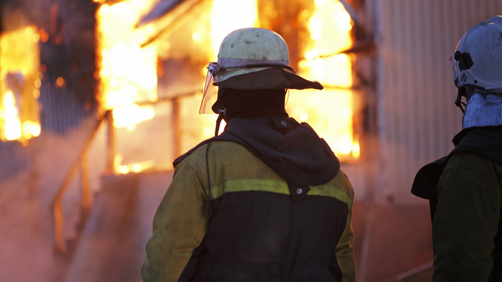 Två brandmän står framför en brinnande byggnad.