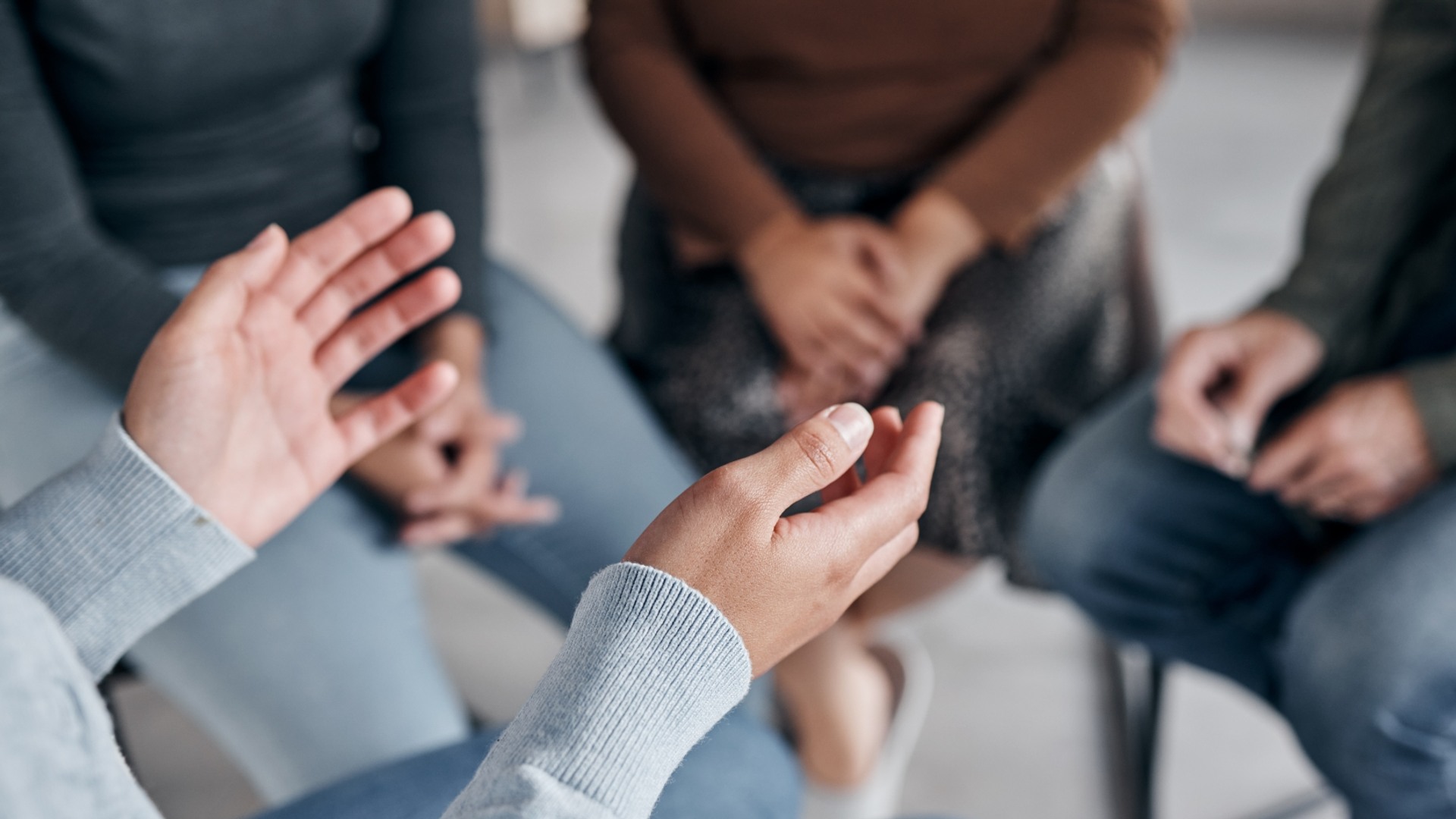 Personer sitter på stolar i en ring. I förgrunden syns en persons händer som gestikulerar.