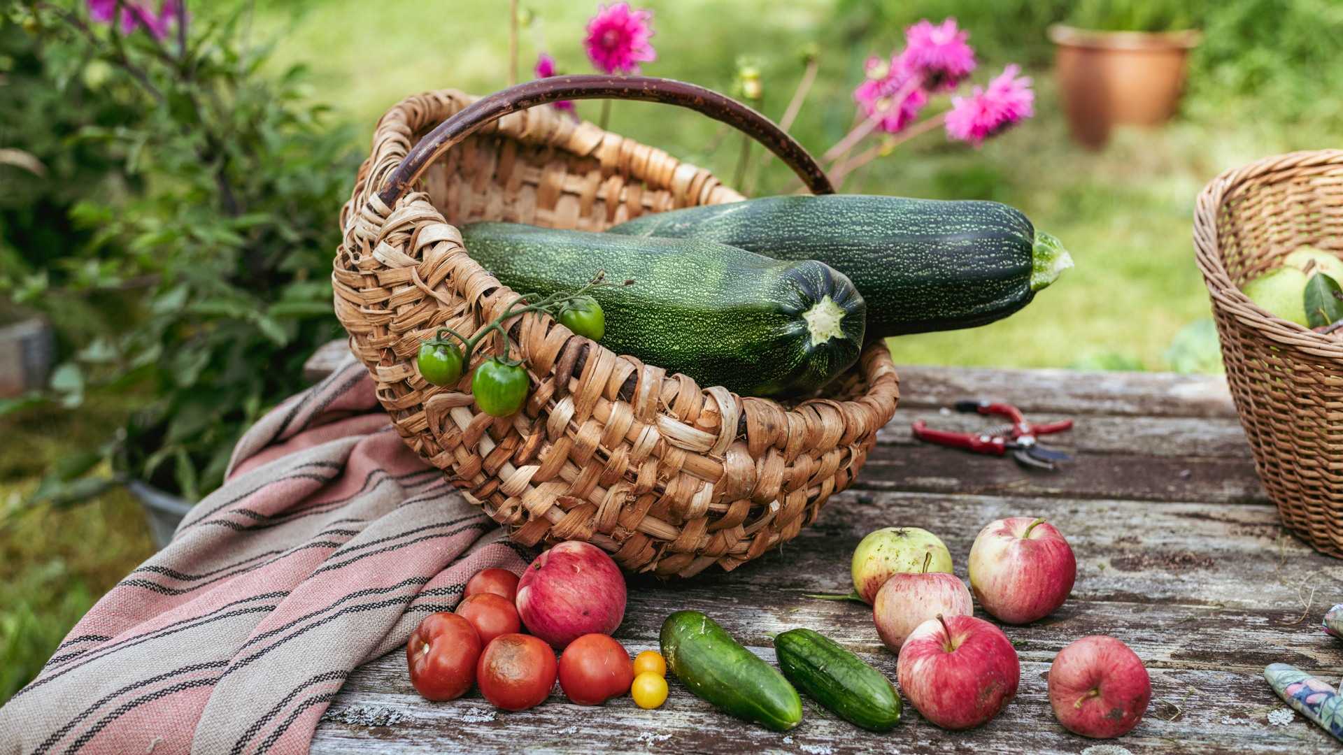 Zucchini och andra grönsaker i en korg på ett träbord utomhus.
