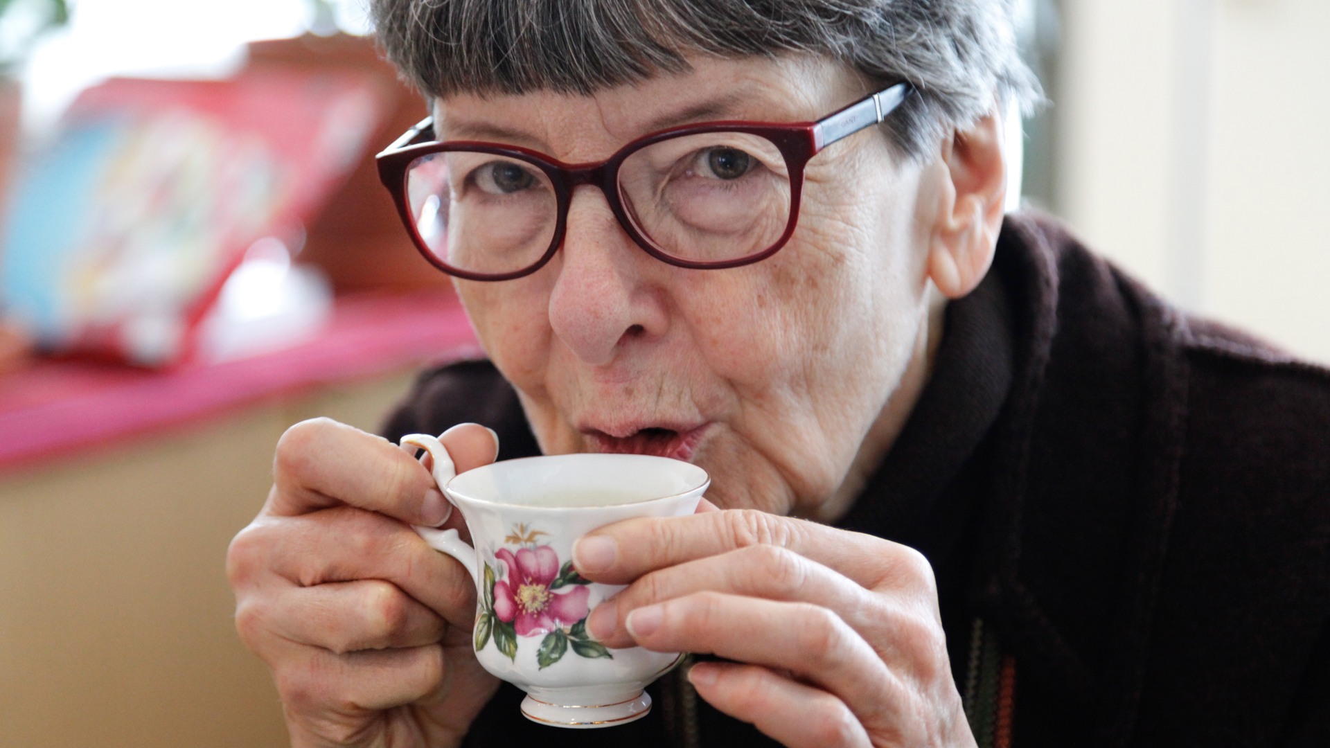Äldre kvinna dricker kaffe ur en liten kopp.